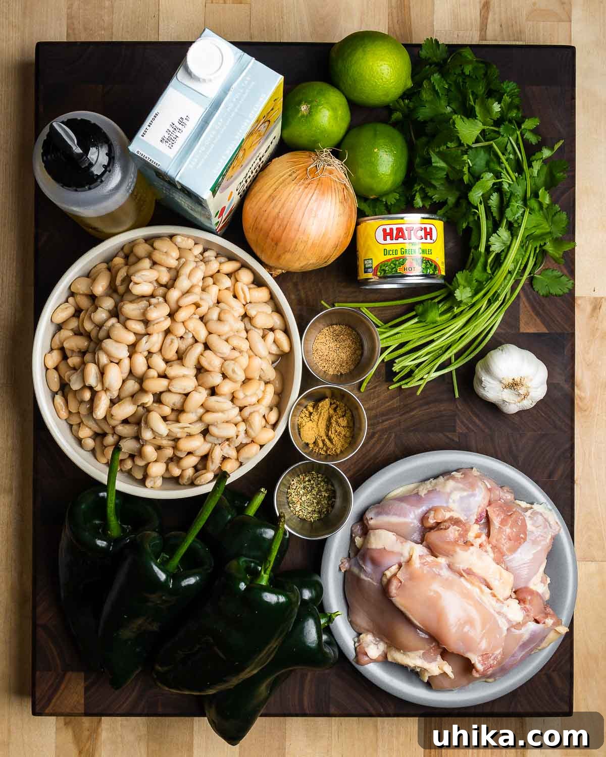 Ingredients for white chicken chili displayed: olive oil, chicken stock, onions, limes, cilantro, green chiles, white beans, spices, garlic, and chicken thighs.