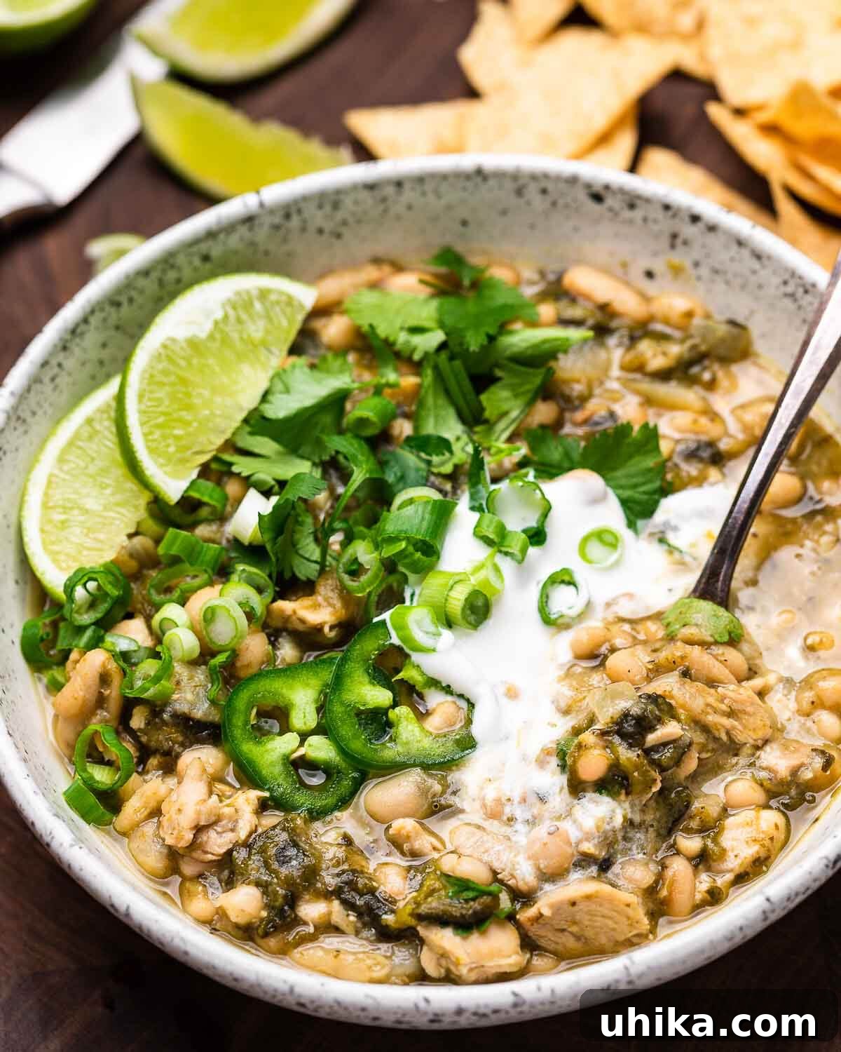 White bowl of white chicken chili topped with limes, green onions, and jalapenos, ready to be enjoyed.