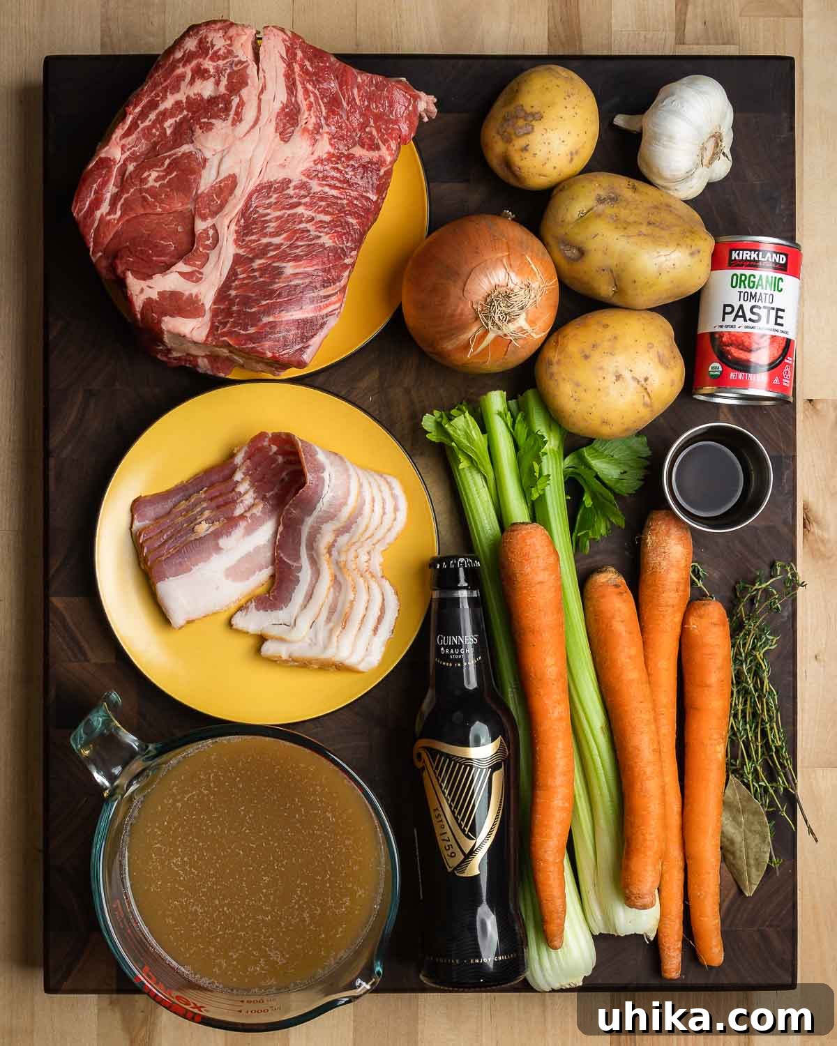 Rich Guinness Beef Stew 3 A vibrant display of fresh ingredients for Guinness beef stew, including beef chuck, chopped onion, potatoes, garlic cloves, rich tomato paste, savory bacon, a bottle of Guinness stout, beef stock, crisp celery, colorful carrots, fragrant herbs like thyme, and a bottle of Worcestershire sauce.