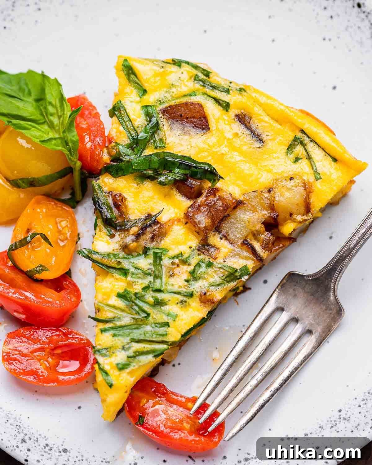 Rustic Potato and Egg Bake 10 A pristine white plate holding a generous slice of golden potato frittata, elegantly garnished with fresh chives and a vibrant scoop of cherry tomato topping, inviting you to savor its flavors.