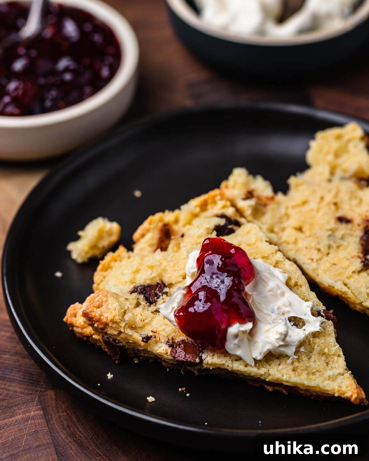 Decadent Chocolate Chip Scones 10 Black plate with chocolate chip scone cut open with jam and clotted cream, ready to be enjoyed.