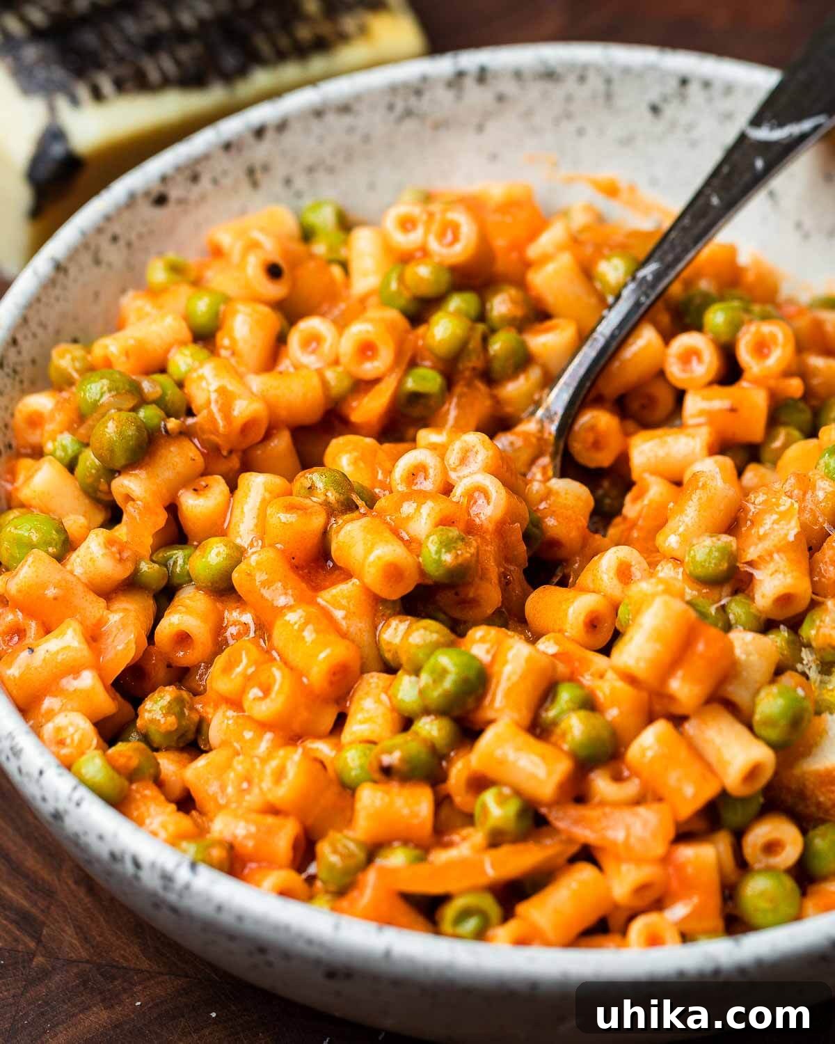 Garden Pea and Tomato Pasta 2 A serving of pasta and peas with red sauce in a white bowl, with a block of Pecorino Romano cheese in the background, ready for grating.