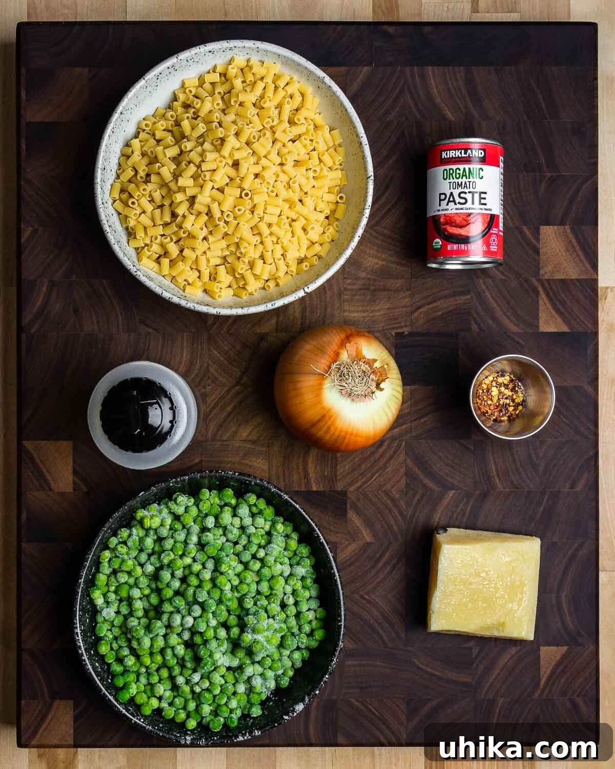 Garden Pea and Tomato Pasta 4 Ingredients laid out: ditalini pasta, tomato paste, olive oil, diced onion, red pepper flakes, frozen peas, and a block of Pecorino Romano.