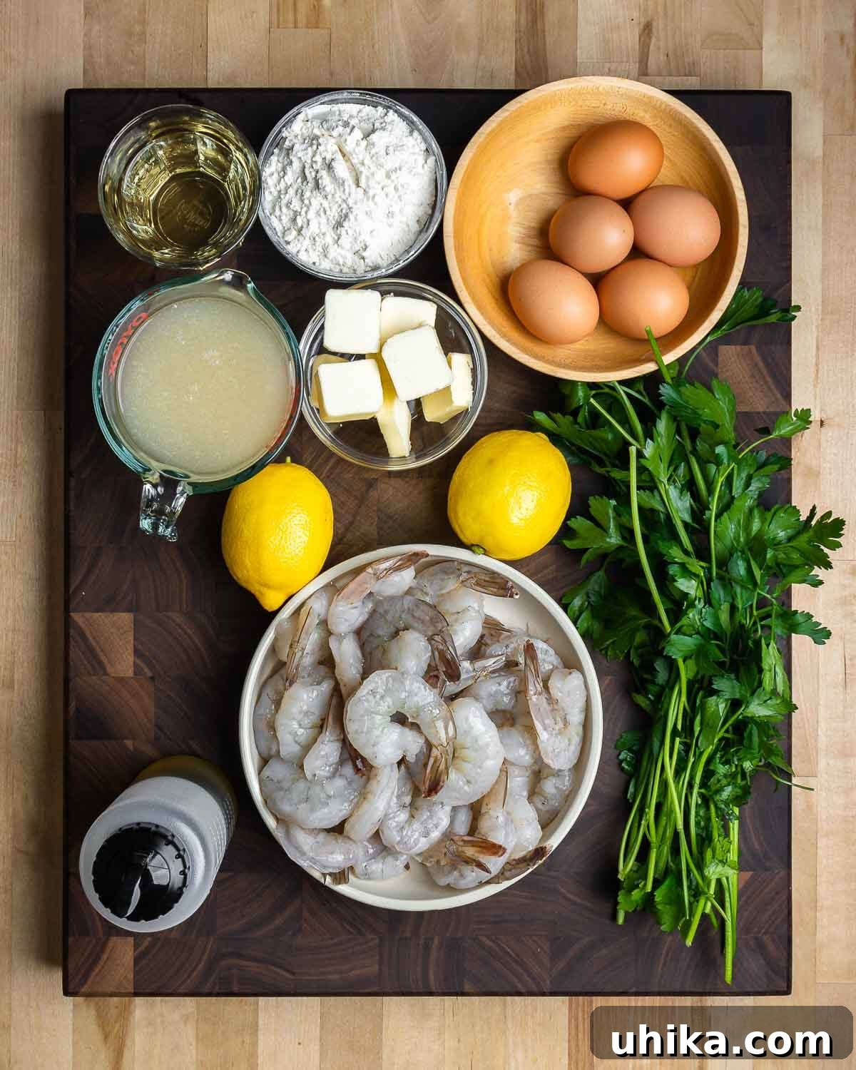Golden Lemon Butter Shrimp 3 Ingredients for Shrimp Francese: white wine, flour, eggs, chicken stock, butter, lemons, parsley, olive oil, and shrimp laid out on a wooden board.