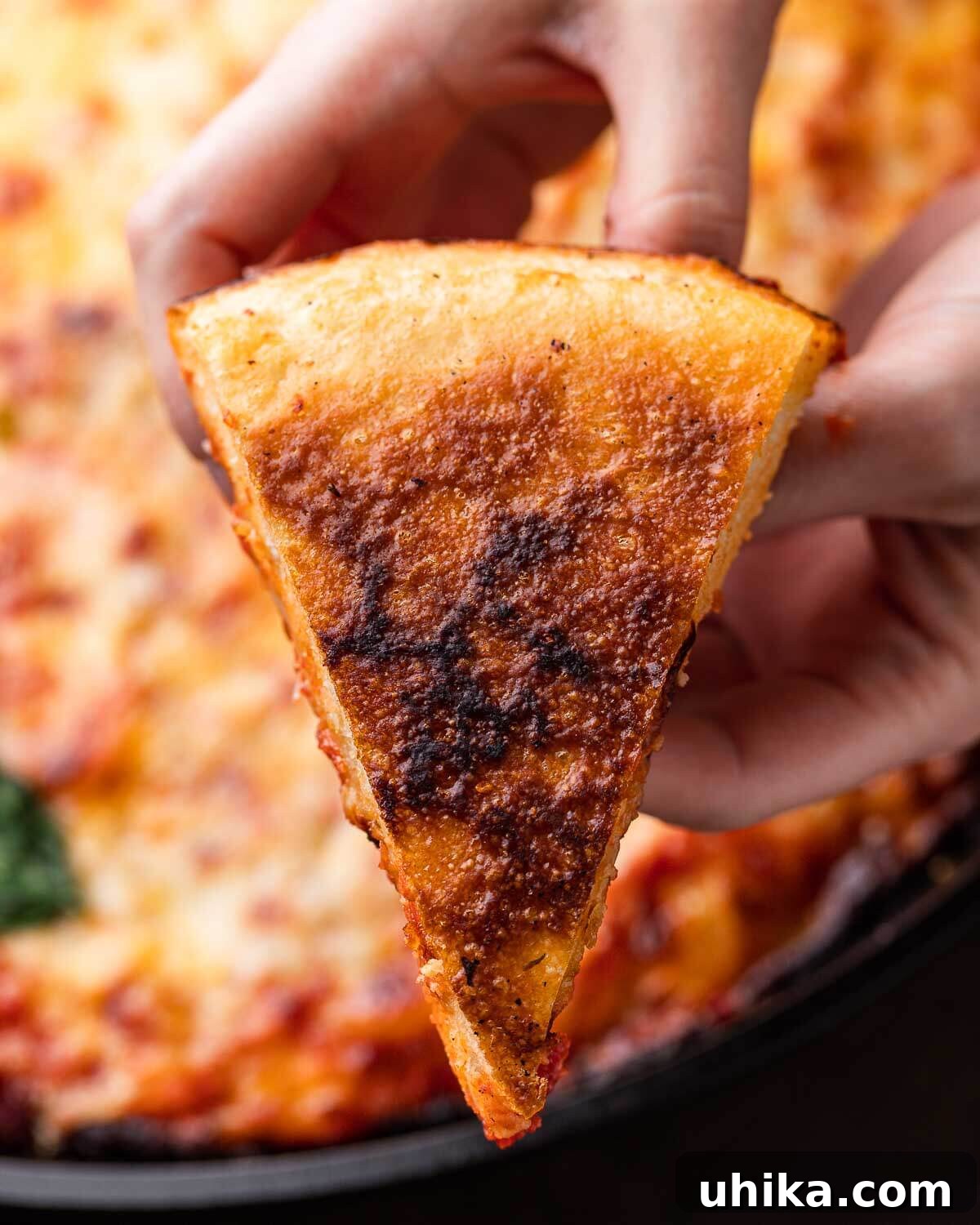 Skillet Pizza Perfection 8 A hand holding a slice of cast iron pizza, turned over to reveal its perfectly golden brown and crispy bottom crust.