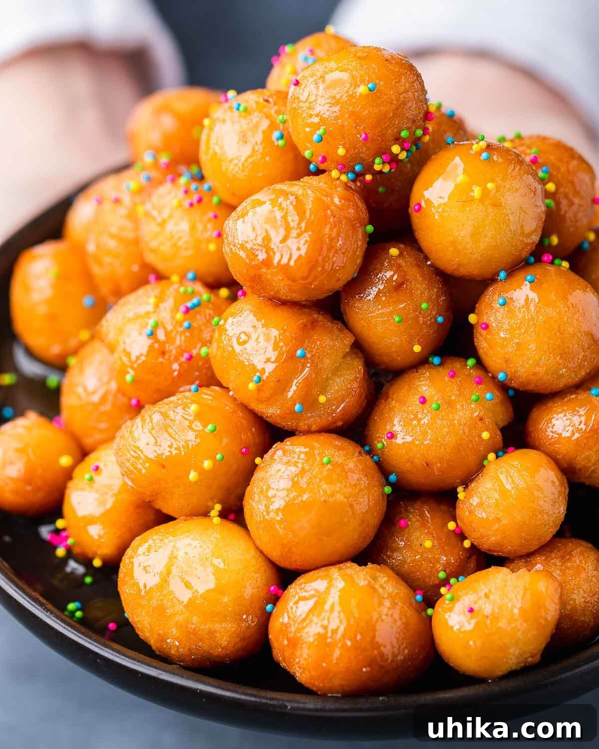 Neapolitan Christmas Honey Bites 2 Hands holding black plate with a mound of struffoli.