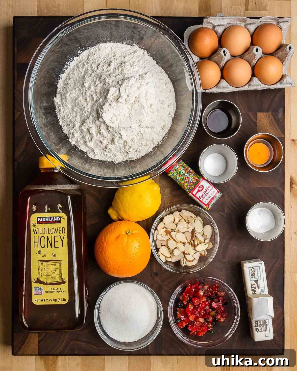 Neapolitan Christmas Honey Bites 3 Ingredients shown: flour, eggs, vanilla, Gran Marnier, salt, baking powder, nonpareils, honey, orange, lemon, almonds, candied fruit, sugar, and butter.