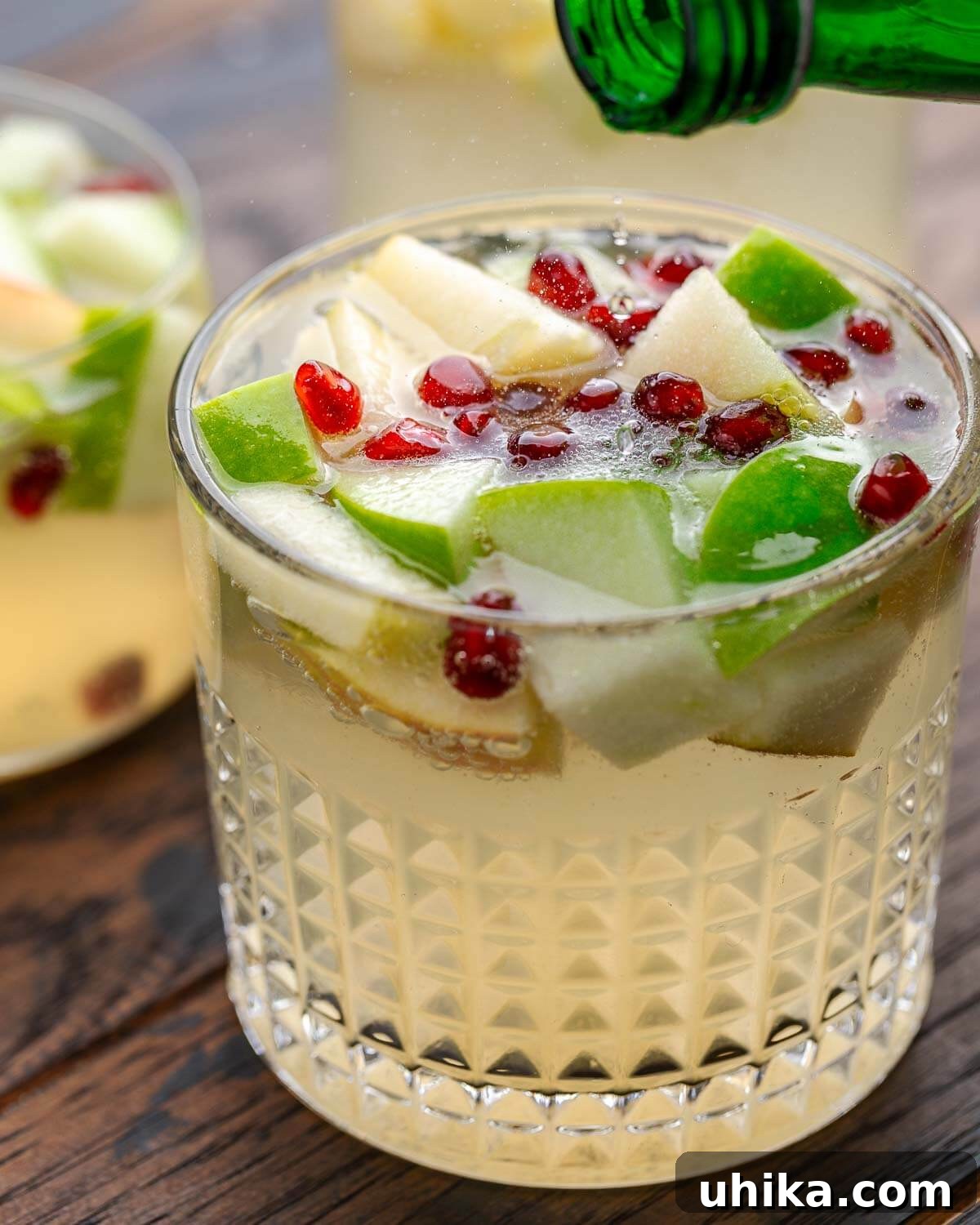 Spiced Autumn Sangria with Pears and Apples 2 Sparkling water being poured into a glass of Thanksgiving White Wine Sangria with apple, pear, and pomegranate garnishes.