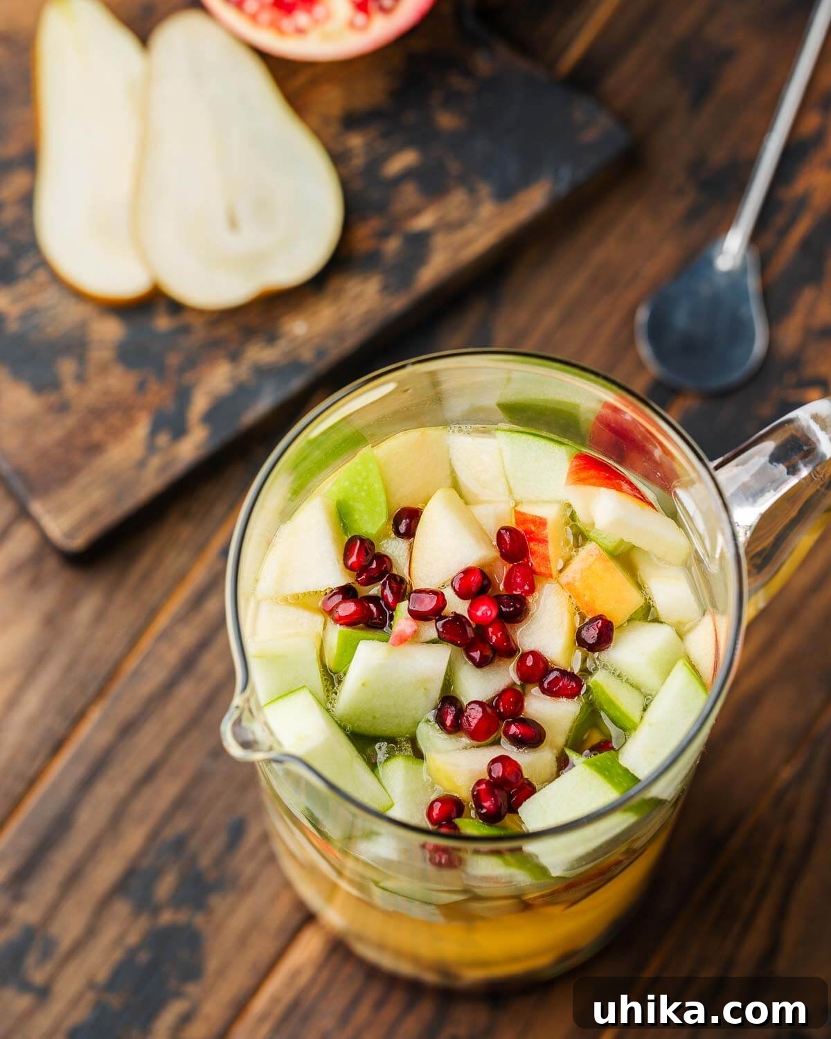 Spiced Autumn Sangria with Pears and Apples 4 Large pitcher filled with Thanksgiving white wine sangria, showing apples, pears, and pomegranate seeds.