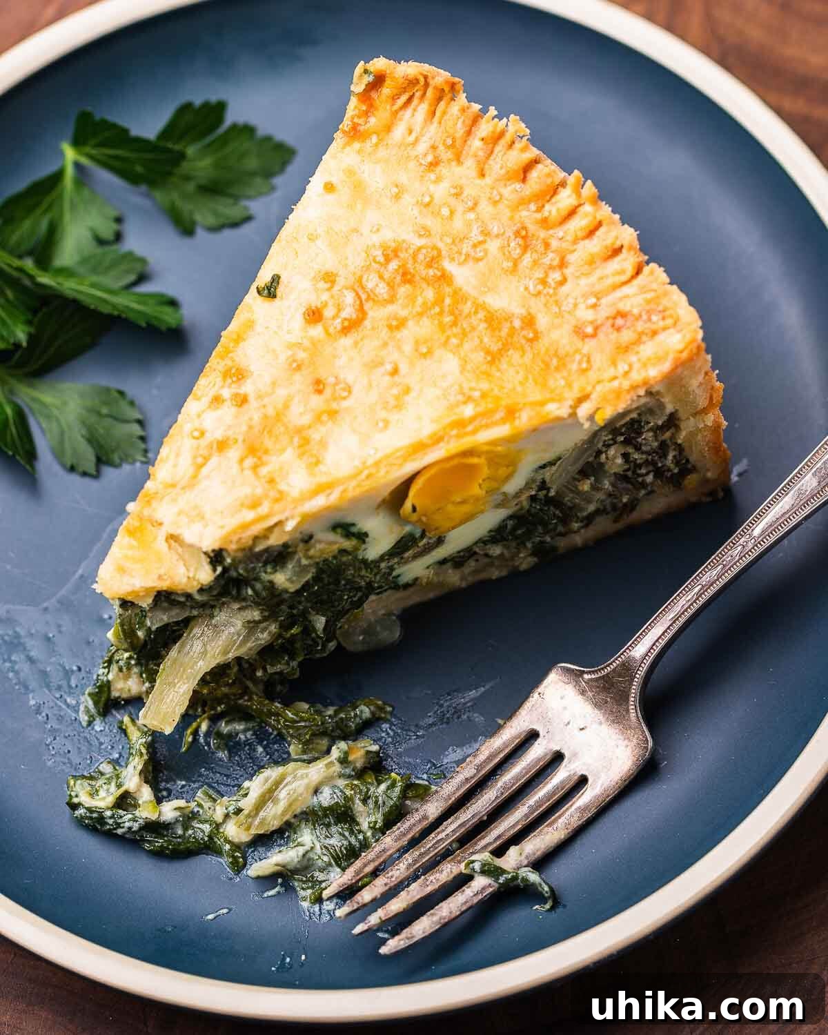 Classic Italian Easter Pie 11 A slice of Torta Pasqualina artfully placed on a blue plate with a fork, highlighting the vibrant green filling and golden crust.