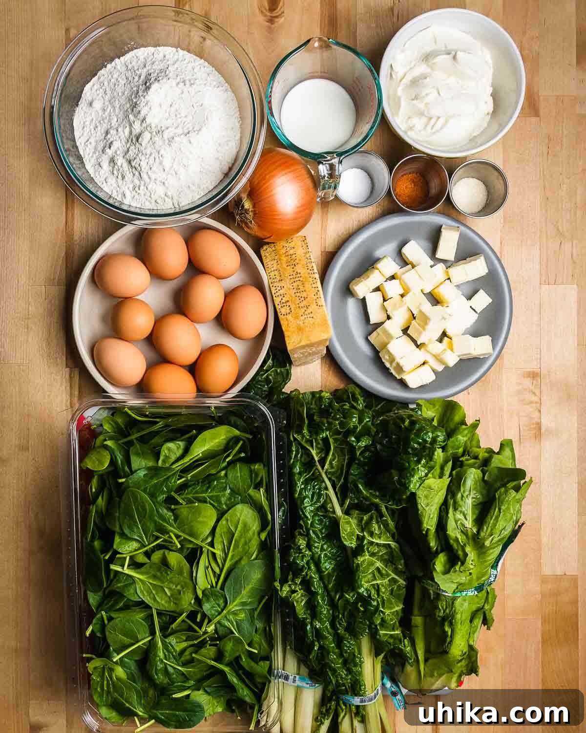 Classic Italian Easter Pie 3 A collection of fresh ingredients laid out for Torta Pasqualina, including flour, milk, creamy ricotta, onion, salt, sugar, nutmeg, fresh eggs, Parmesan cheese, butter, spinach, Swiss chard, and escarole.