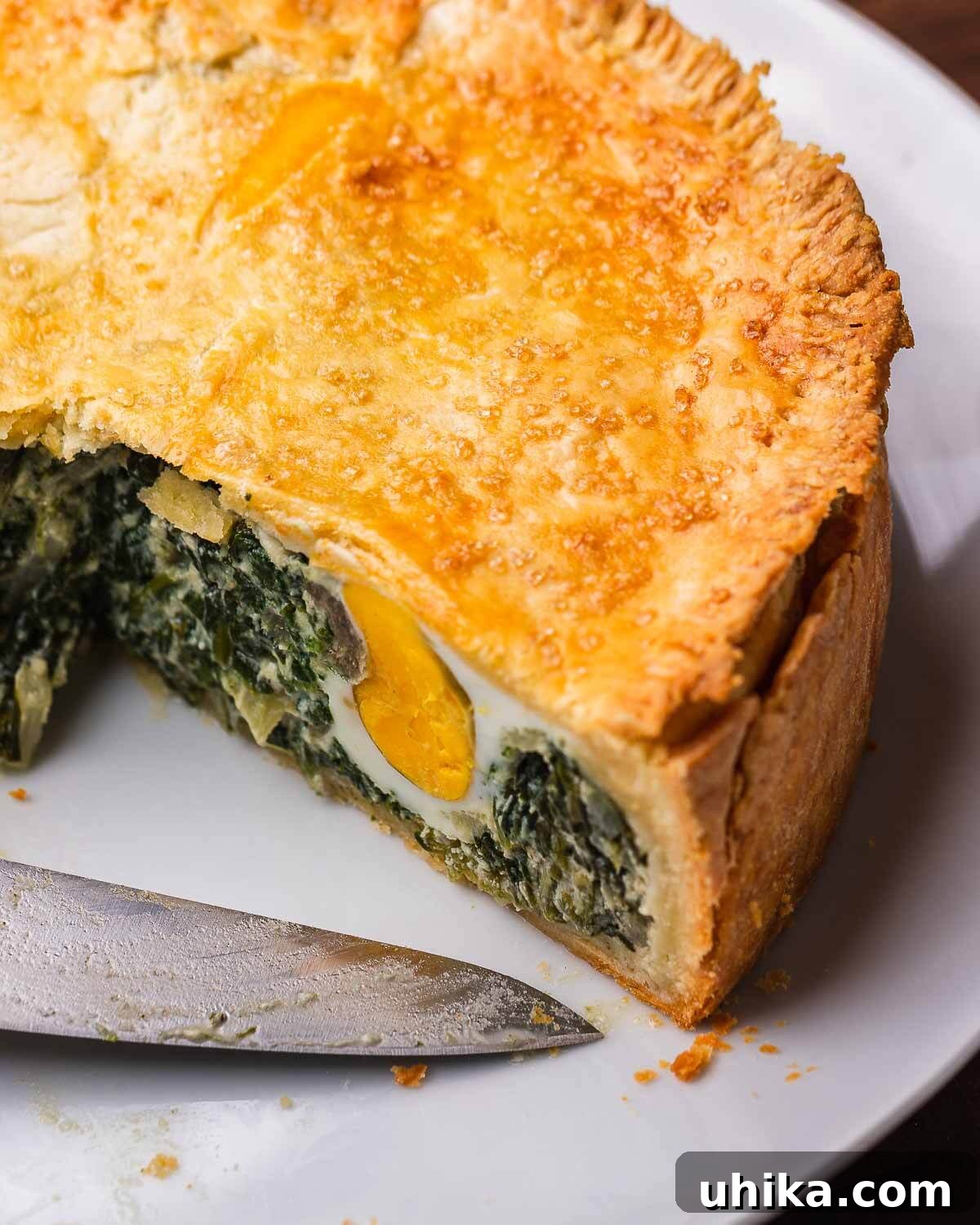 Classic Italian Easter Pie 10 A whole Torta Pasqualina, freshly baked to a golden brown, presented on a white platter with a serving knife beside it.