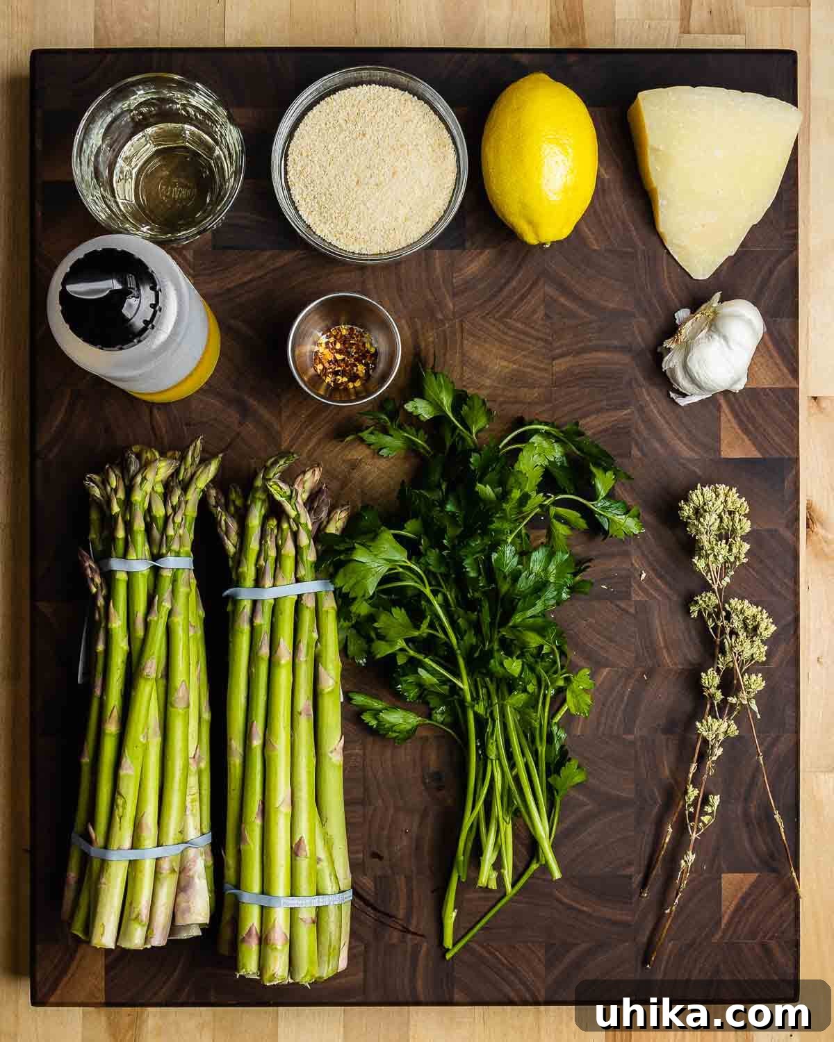 Crispy Parmesan Asparagus Bake 3 A colorful array of ingredients for baked asparagus: white wine, breadcrumbs, fresh lemon, Pecorino cheese, olive oil, hot red pepper flakes, garlic cloves, green asparagus spears, fresh parsley, and Sicilian oregano.