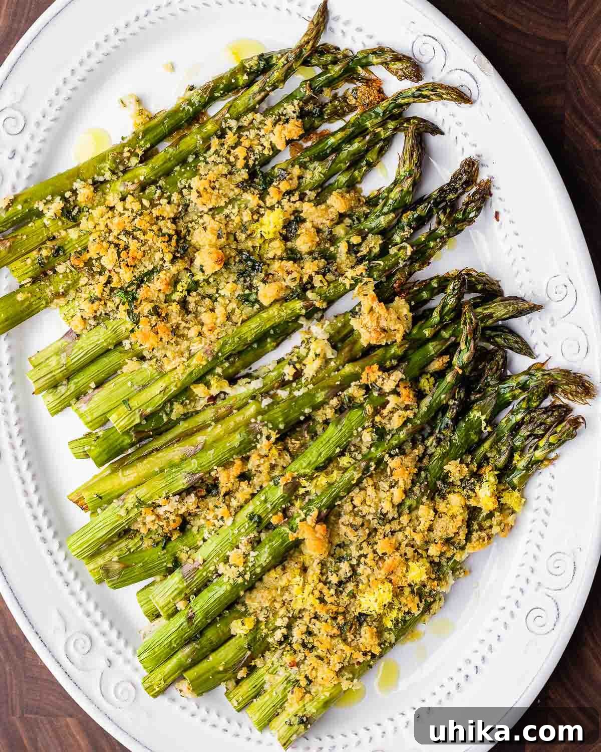 Crispy Parmesan Asparagus Bake 9 Overhead shot of baked asparagus with cheese and breadcrumbs presented beautifully on a white platter, garnished and ready to eat.
