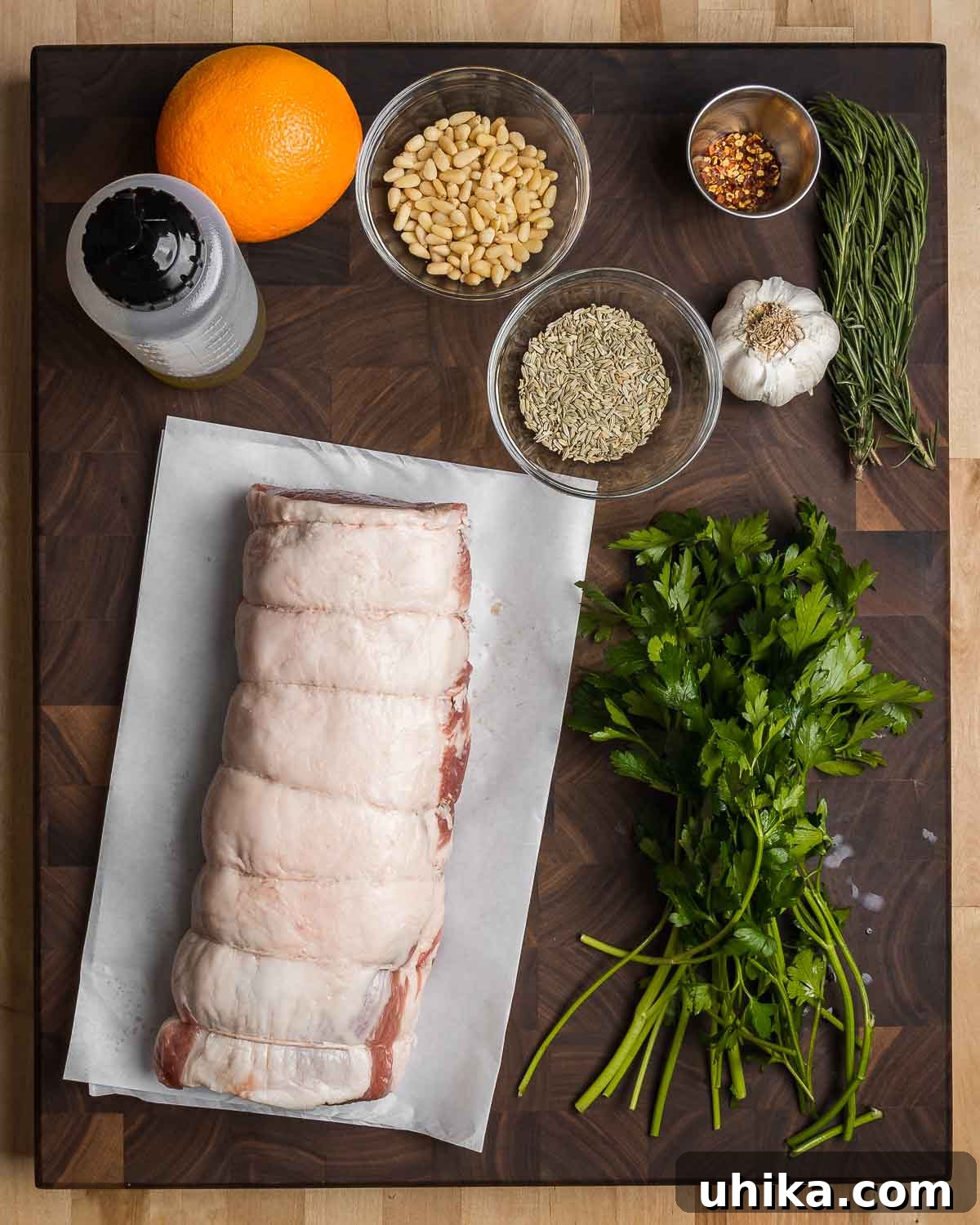 Classic Italian Stuffed Pork Loin 4 Ingredients shown: fresh orange, olive oil, pine nuts, fennel seeds, hot red pepper flakes, garlic cloves, fresh rosemary sprigs, flat-leaf parsley, and a tied pork loin ready for stuffing.