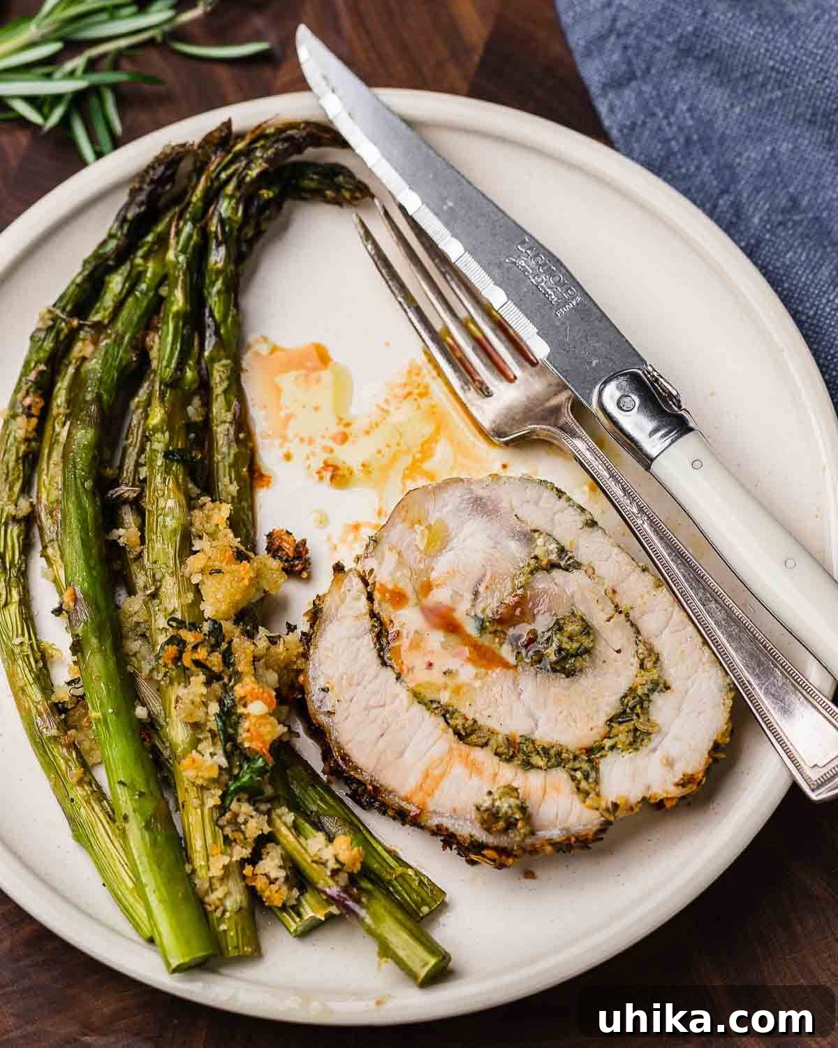 Classic Italian Stuffed Pork Loin 10 Overhead shot of sliced stuffed pork loin and green asparagus on a white plate, ready to be served.