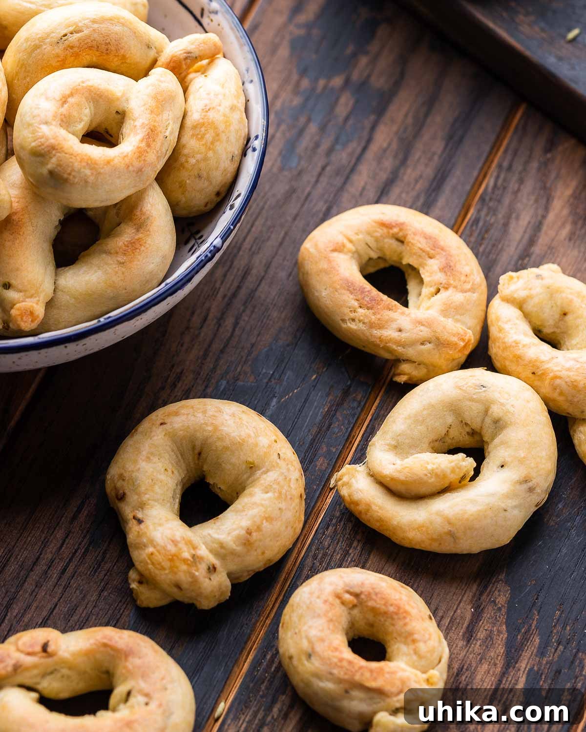 Taralli 9 Taralli artistically arranged on a rustic walnut board with a bowl of more taralli in the background, showcasing their golden-brown color and perfect loop shape.