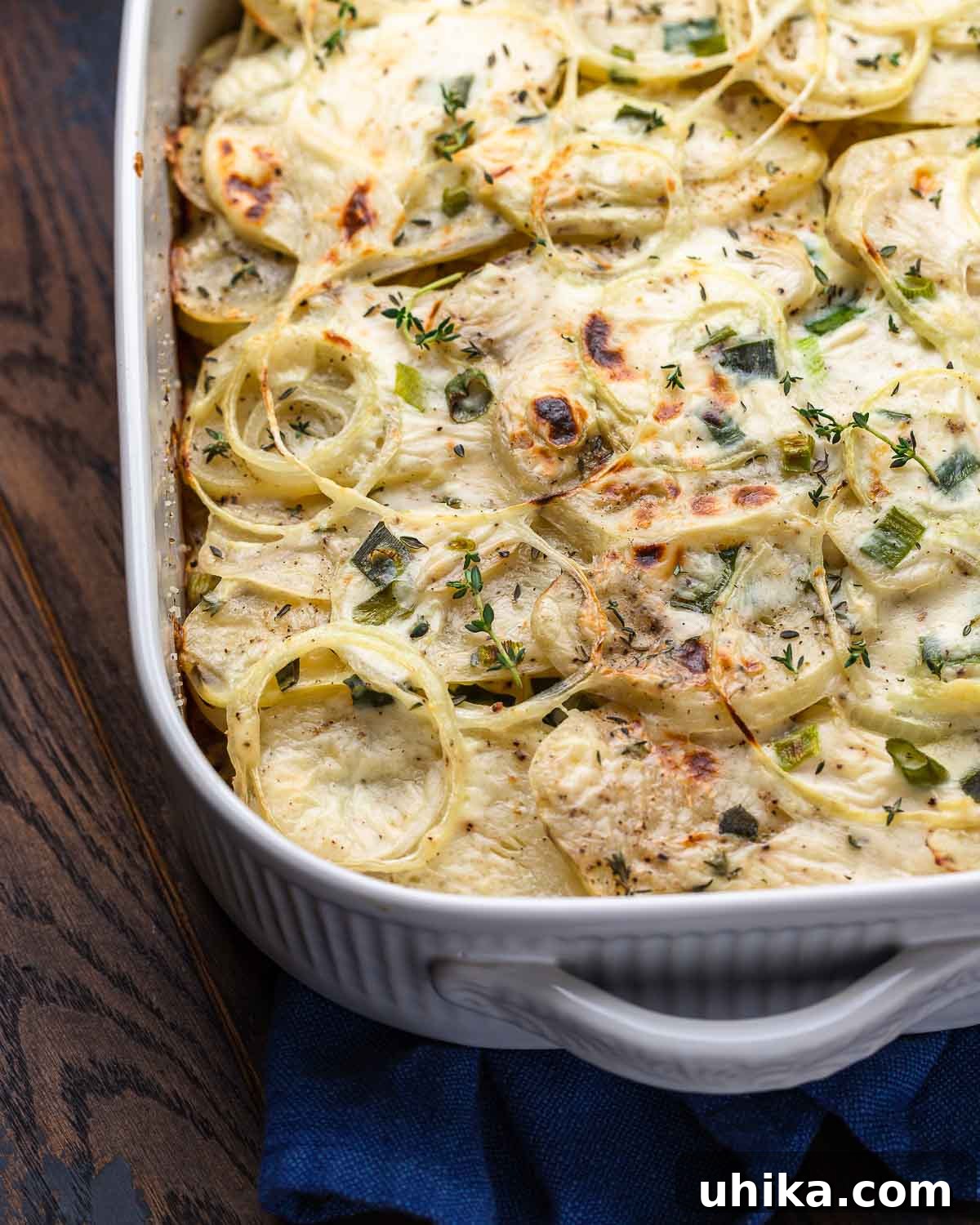 Ultimate Creamy Potato Gratin 2 A white baking dish filled with golden-brown scalloped potatoes, ready to be served on a rustic wooden board.