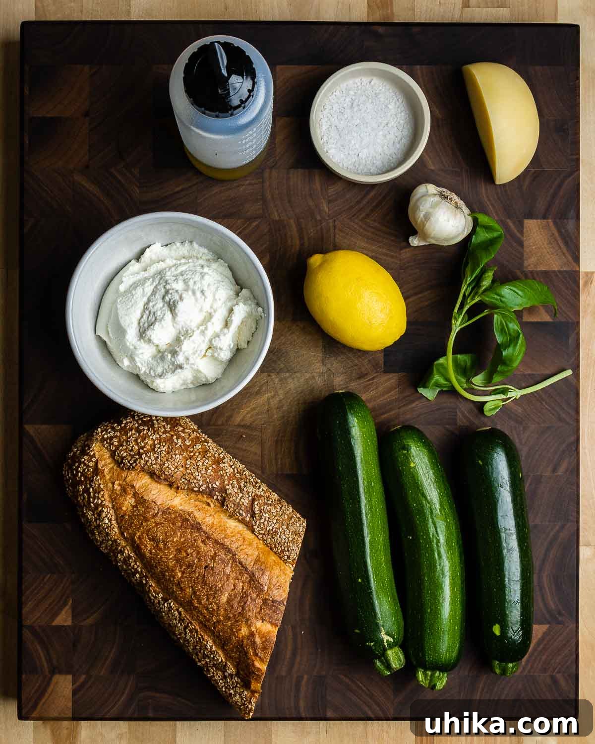 Zucchini Bruschetta Delights 3 A flat lay photograph showcasing all the ingredients for Zucchini Bruschetta: extra virgin olive oil, flaky sea salt, a head of garlic, caciocavallo cheese, fresh ricotta, a lemon, basil leaves, crusty bread, and fresh zucchini.