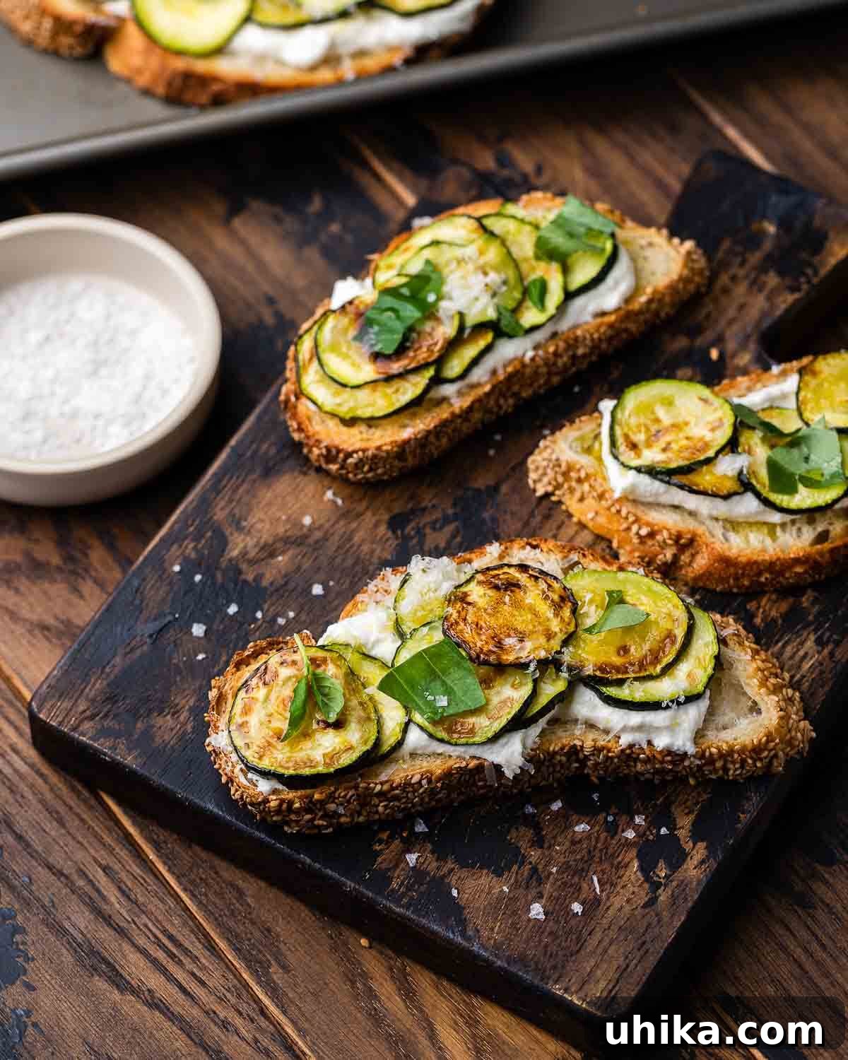 Zucchini Bruschetta Delights 7 Beautifully arranged Zucchini Bruschetta on a wooden board, with a small bowl of flaky sea salt in the softly blurred background.