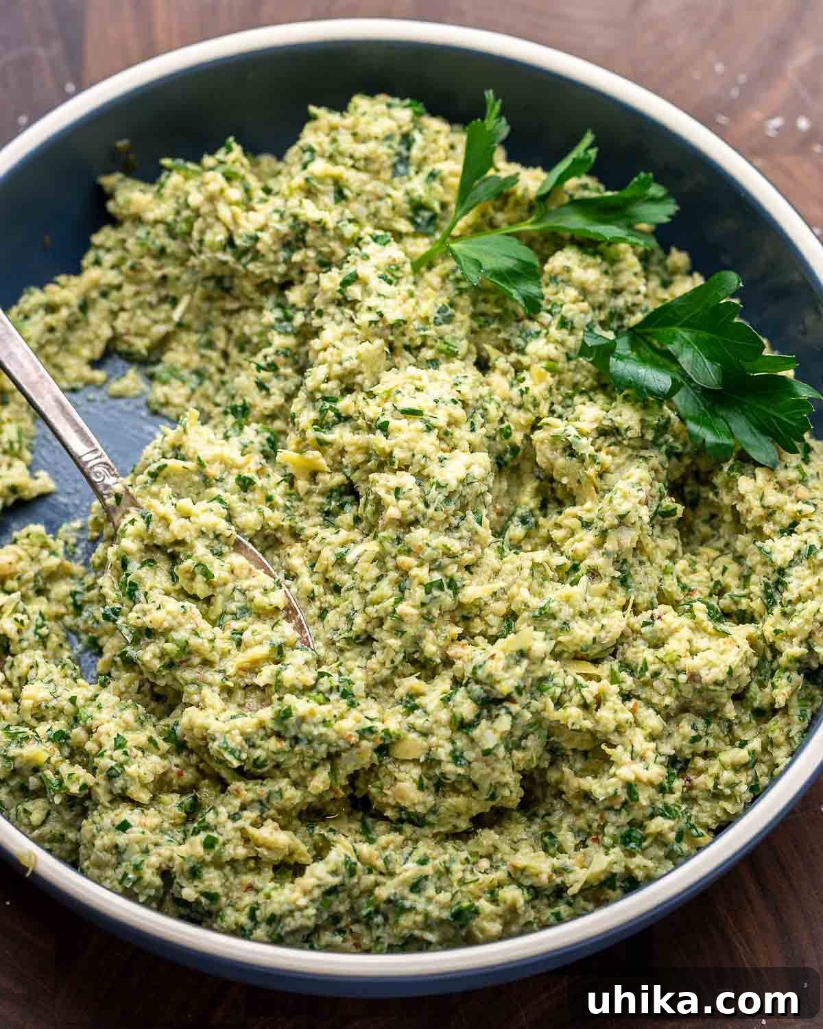 Vibrant Artichoke Pesto 7 Artichoke pesto in a rustic blue bowl, sitting on a natural walnut cutting board, with fresh parsley garnish.