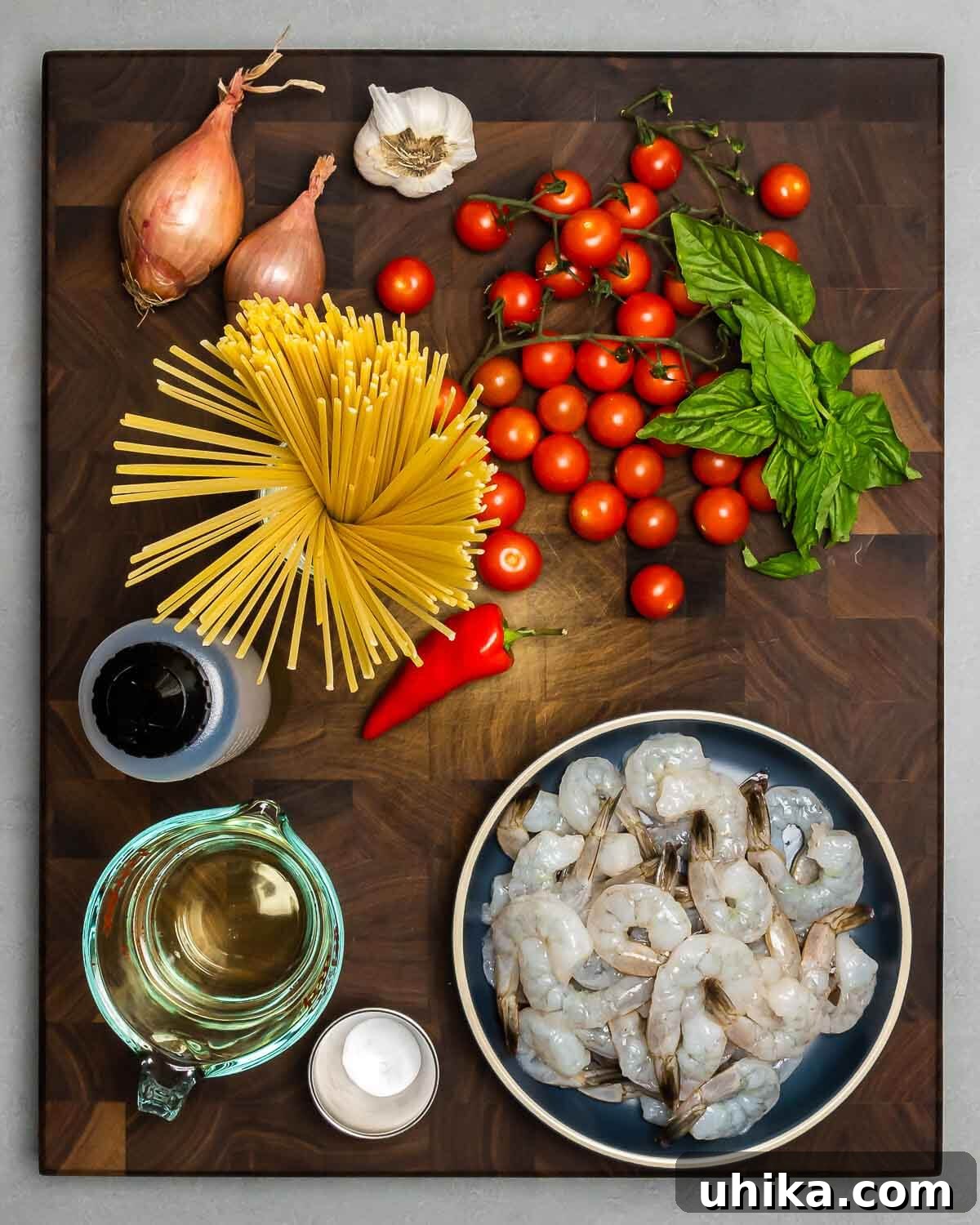 Garlic-Kissed Shrimp Tomato Basil Pasta 3 Carefully arranged ingredients for Shrimp Tomato Basil Pasta: fresh shallots, garlic cloves, vibrant cherry tomatoes, green basil leaves, dry linguine pasta, a red chili pepper, golden olive oil, a bottle of white wine, a small bowl of baking soda, and raw shrimp.