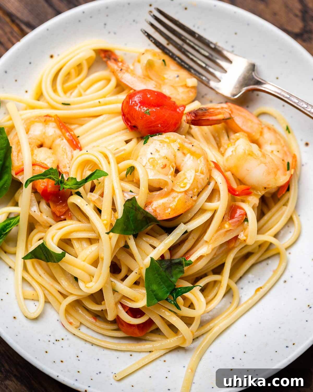 Garlic-Kissed Shrimp Tomato Basil Pasta 7 A serving of Shrimp Tomato Basil Pasta on a white plate with a fork, garnished with fresh basil.