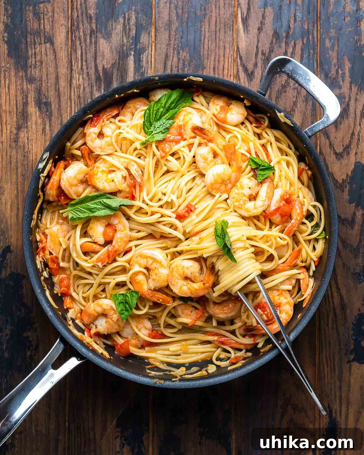 Garlic-Kissed Shrimp Tomato Basil Pasta 8 Overhead view of Shrimp Tomato Basil Pasta served in a black pan on a wooden board, garnished with fresh basil.