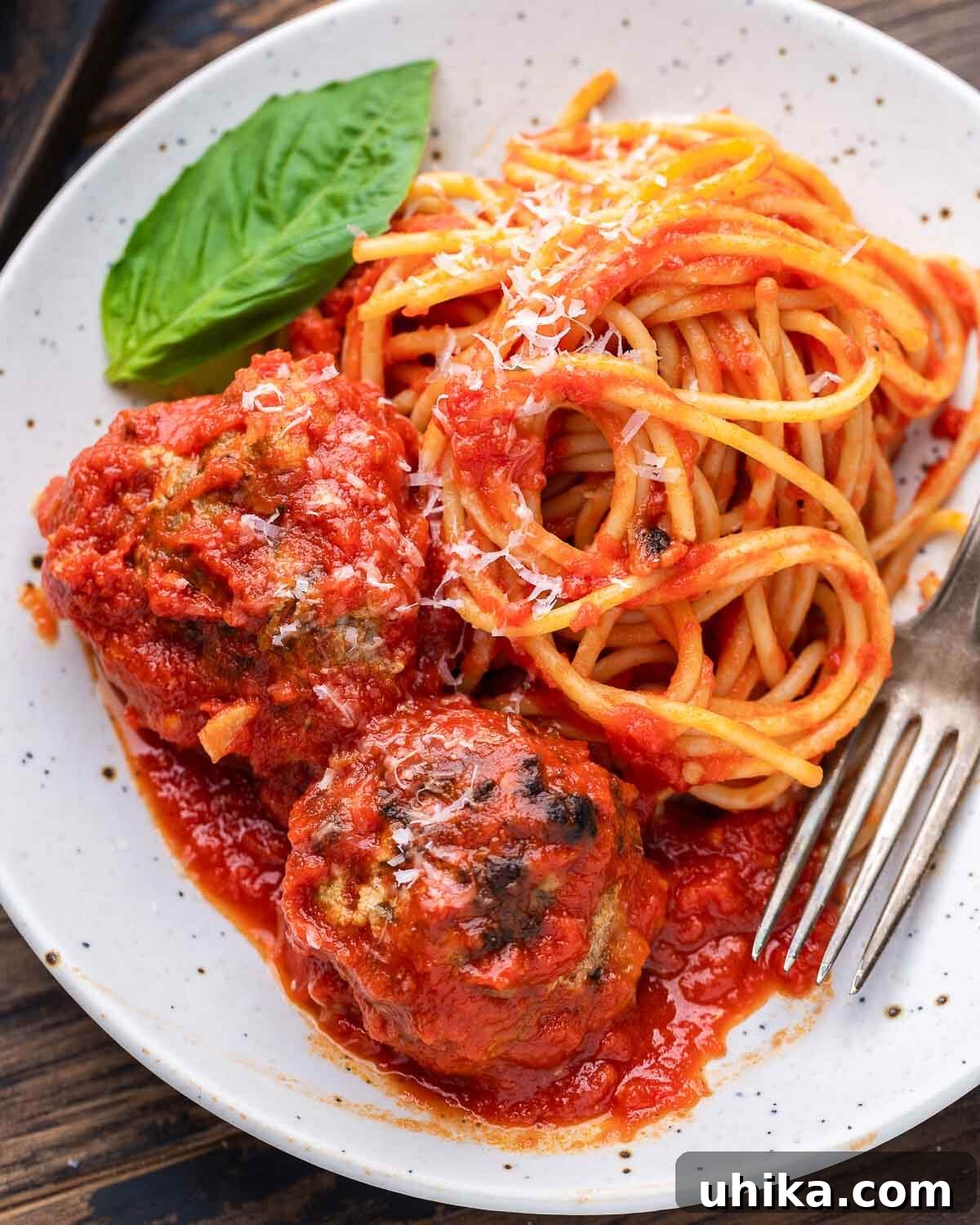Mama's Meatball Magic 2 Spaghetti and meatballs on a pristine white plate, elegantly garnished with fresh basil, ready to be served.