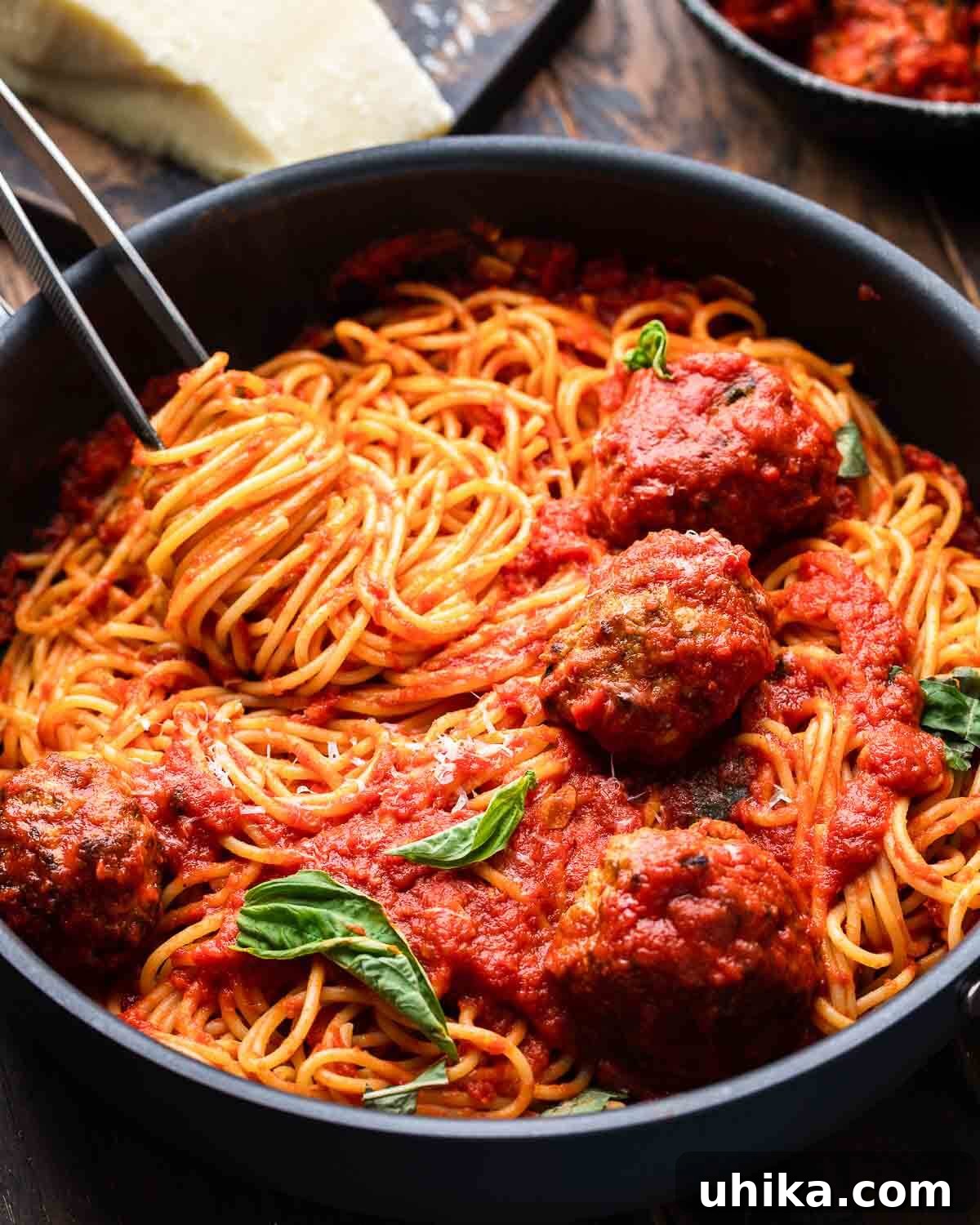 Mama's Meatball Magic 9 A rustic culinary scene featuring spaghetti and meatballs simmering in a black pan, with a block of cheese and a bowl of raw meatballs in the blurred background.