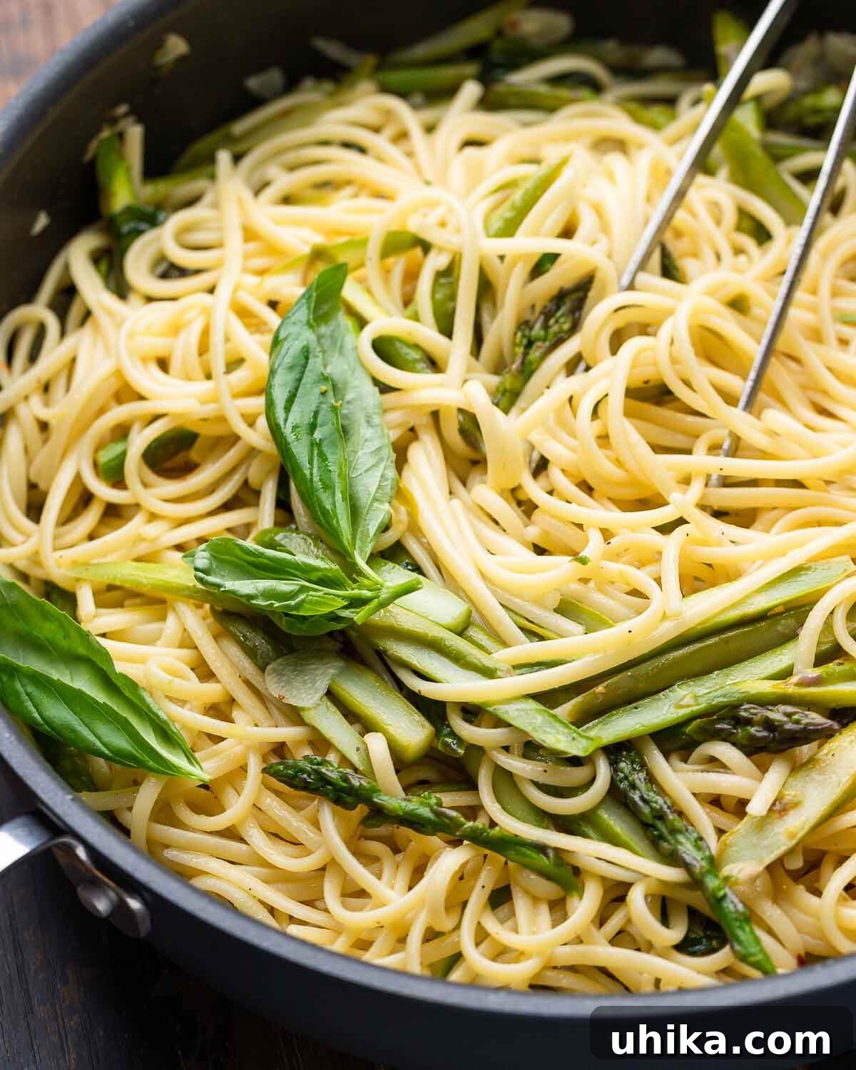 Closeup shot of lemon basil asparagus pasta in black pan, showcasing vibrant green asparagus and fresh basil.