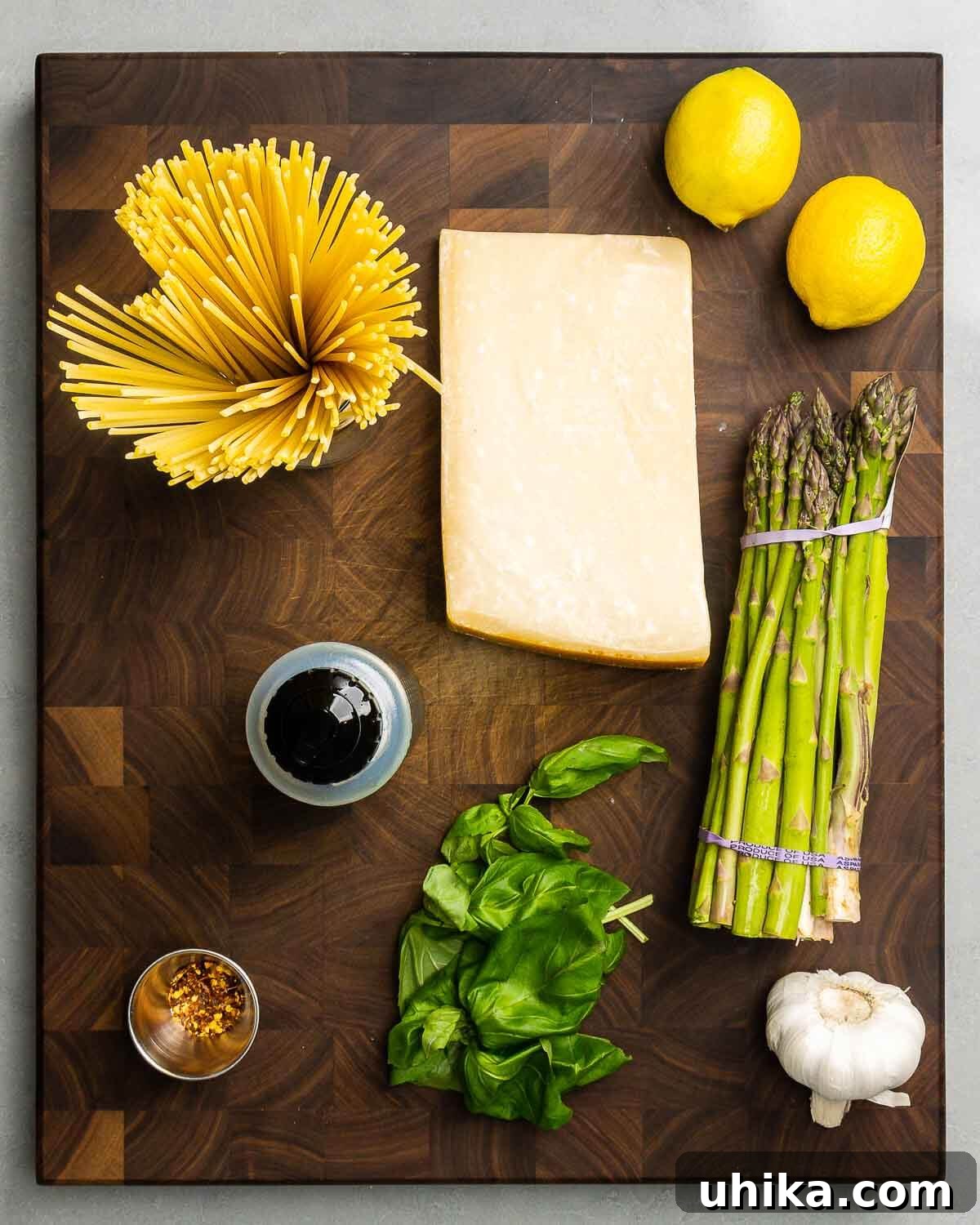 Ingredients shown: spaghetti, parmesan, lemons, asparagus, olive oil, hot red pepper flakes, basil, and garlic arranged artfully on a surface.
