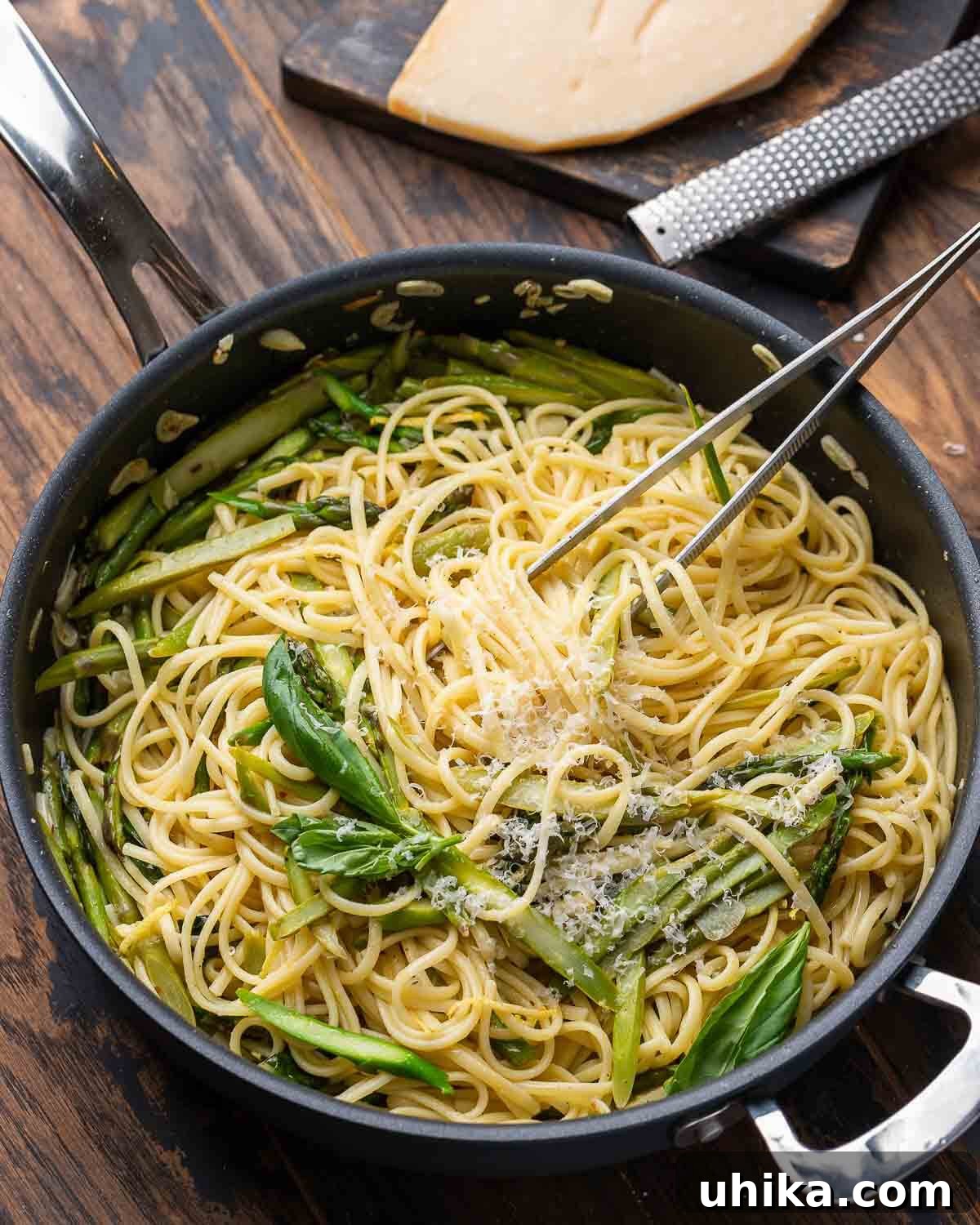 Black pan with lemon asparagus pasta along with block of parmesan cheese in the background, highlighting the rustic appeal.