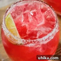 A prickly pear margarita over ice in a glass with a salted rim, a lime wedge for garnish.