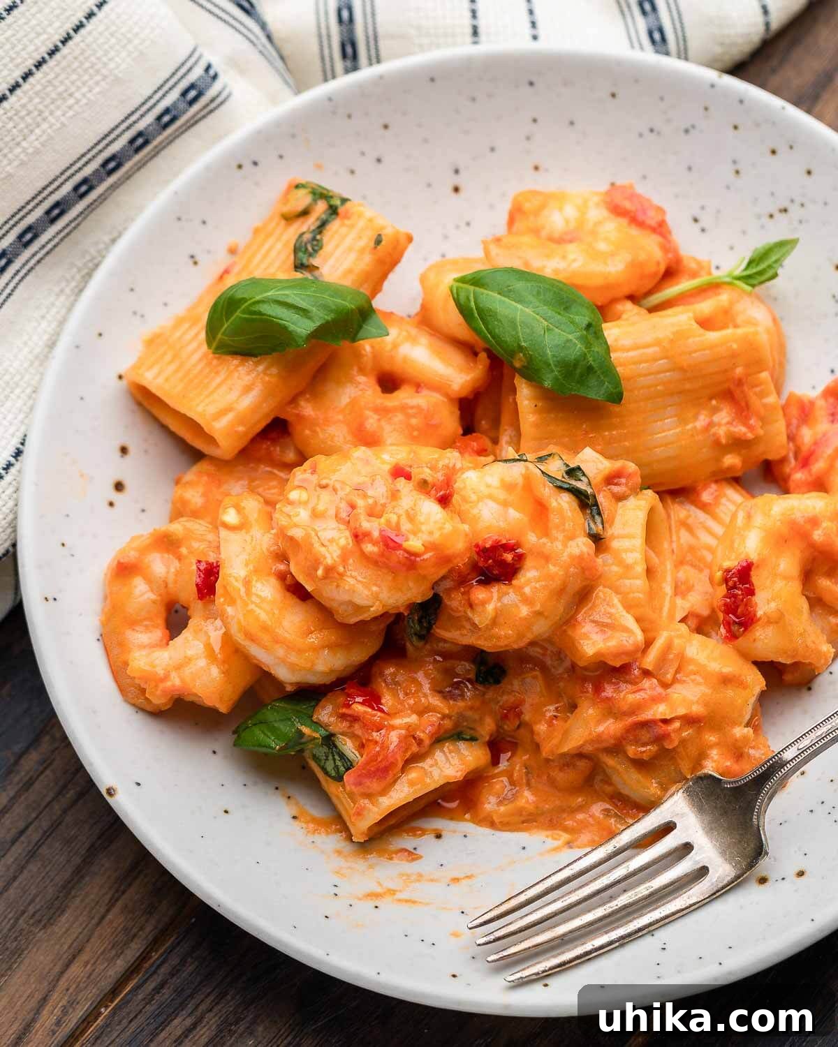 A white plate filled with generous serving of Shrimp alla Vodka, garnished with fresh basil, next to a simple white napkin.