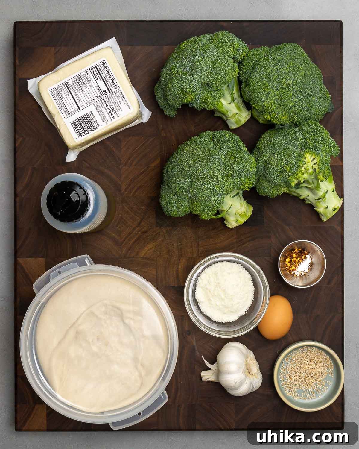 Broccoli Pinwheels 3 Ingredients for broccoli rolls displayed: mozzarella cheese, fresh broccoli crowns, olive oil, Pecorino Romano cheese, eggs, hot red pepper flakes, minced garlic, sesame seeds, and pizza dough.