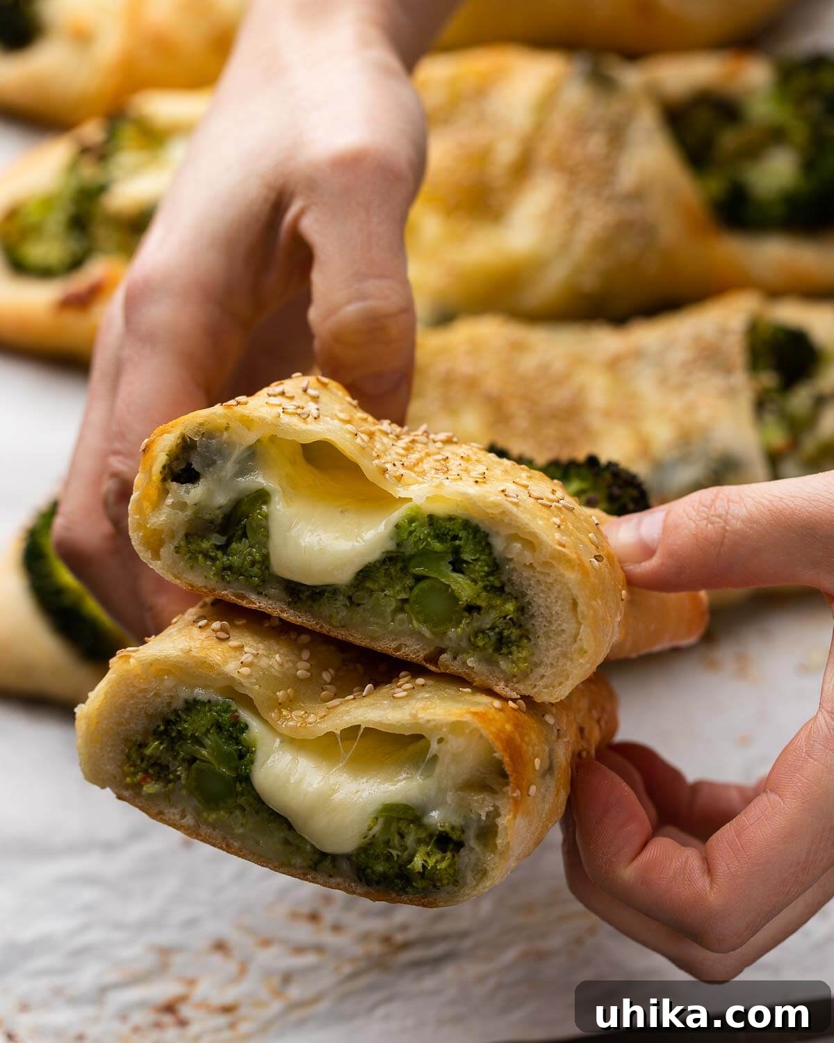 Broccoli Pinwheels 9 Hands holding a freshly cut open broccoli roll, revealing the hot, cheesy, and garlicky broccoli filling inside.