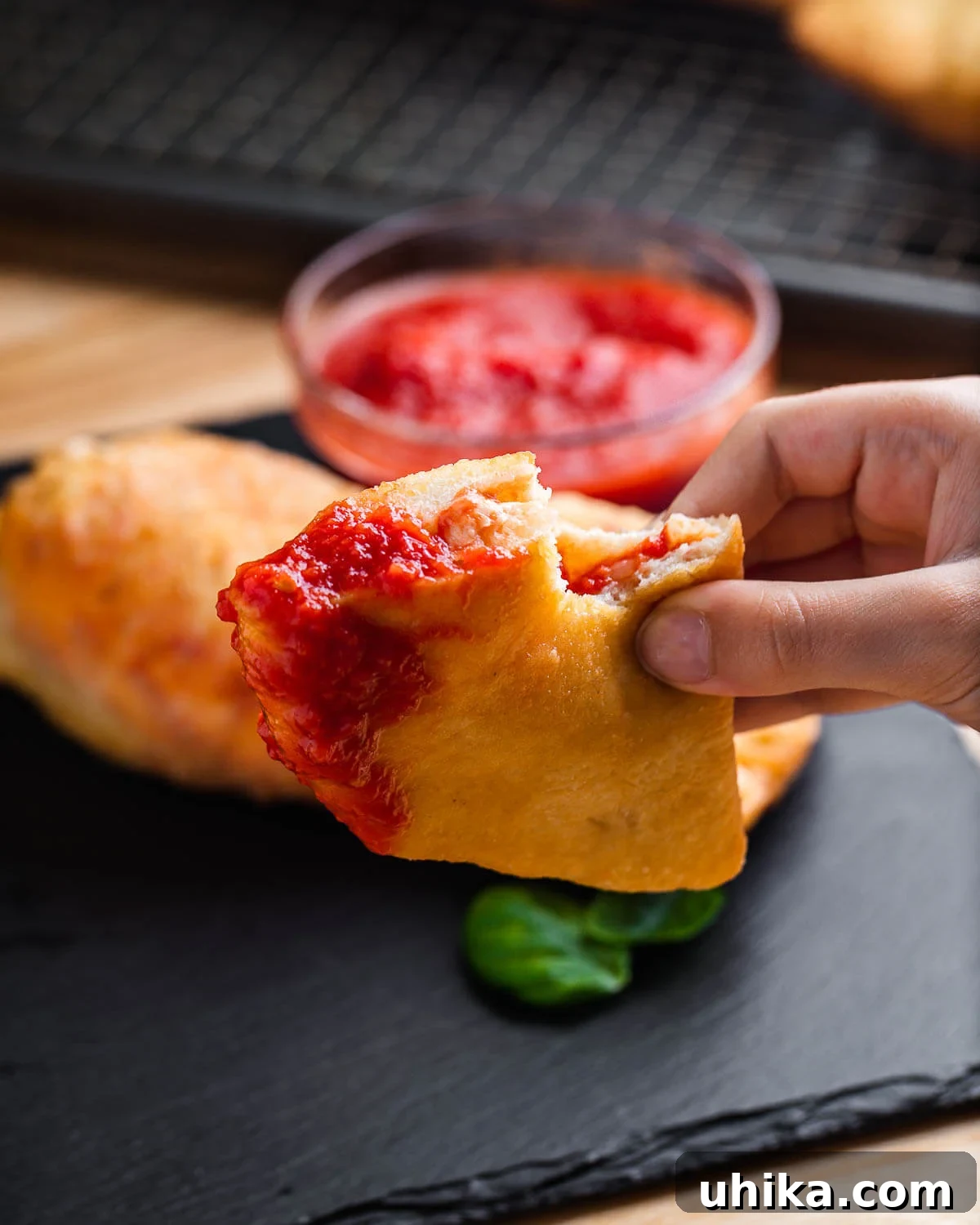Crispy Italian Panzerotti 10 Hands holding a freshly fried panzerotti, dipped into a small bowl of rich red marinara sauce, with a few basil leaves.