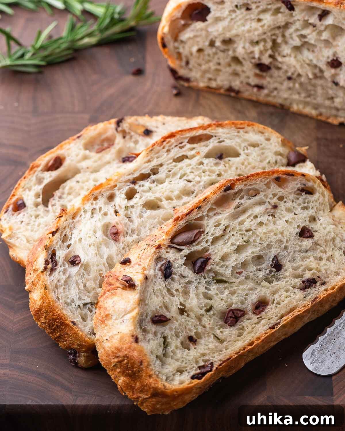 Mediterranean Olive Bread 8 Three slices of olive bread on walnut cutting board with rosemary and rest of the loaf in the background.