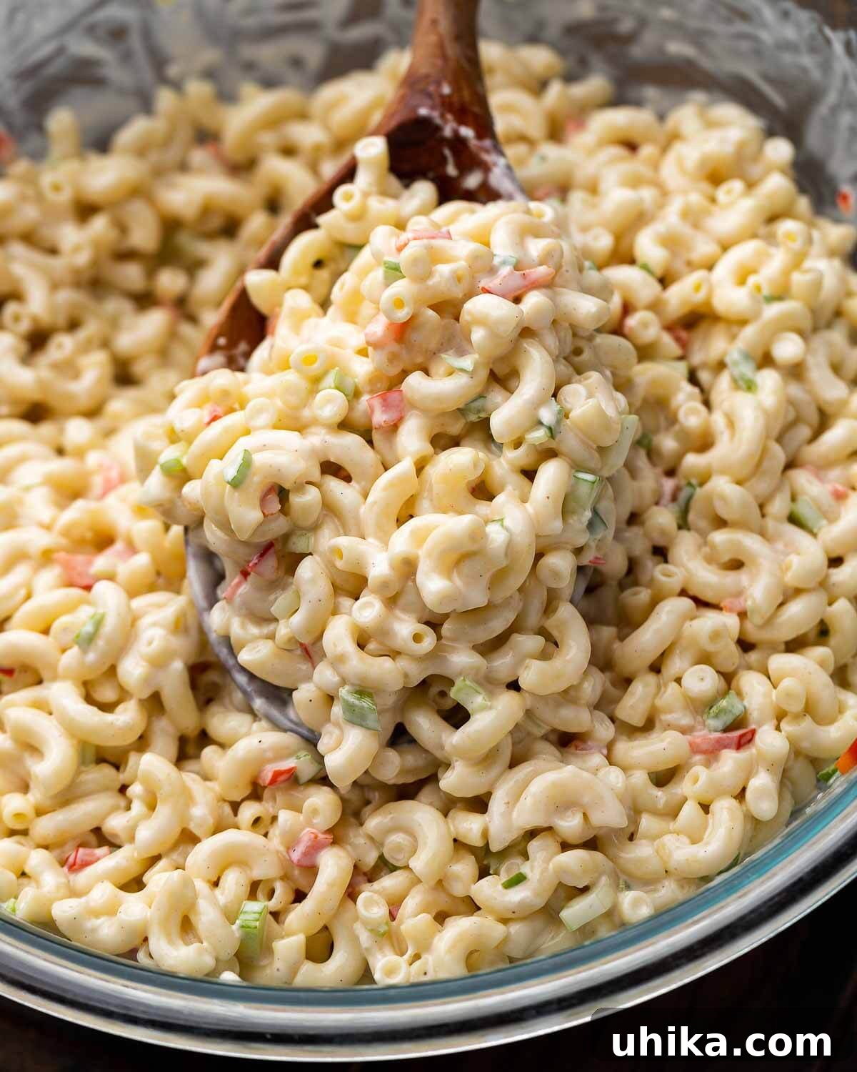 Deli macaroni salad in glass bowl with wooden spoon.