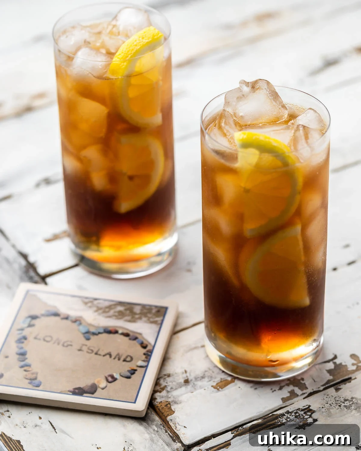 Long Island Iced Tea 2 Two glasses of Long Island iced tea along with a coaster of Long Island, garnished with lemon slices.