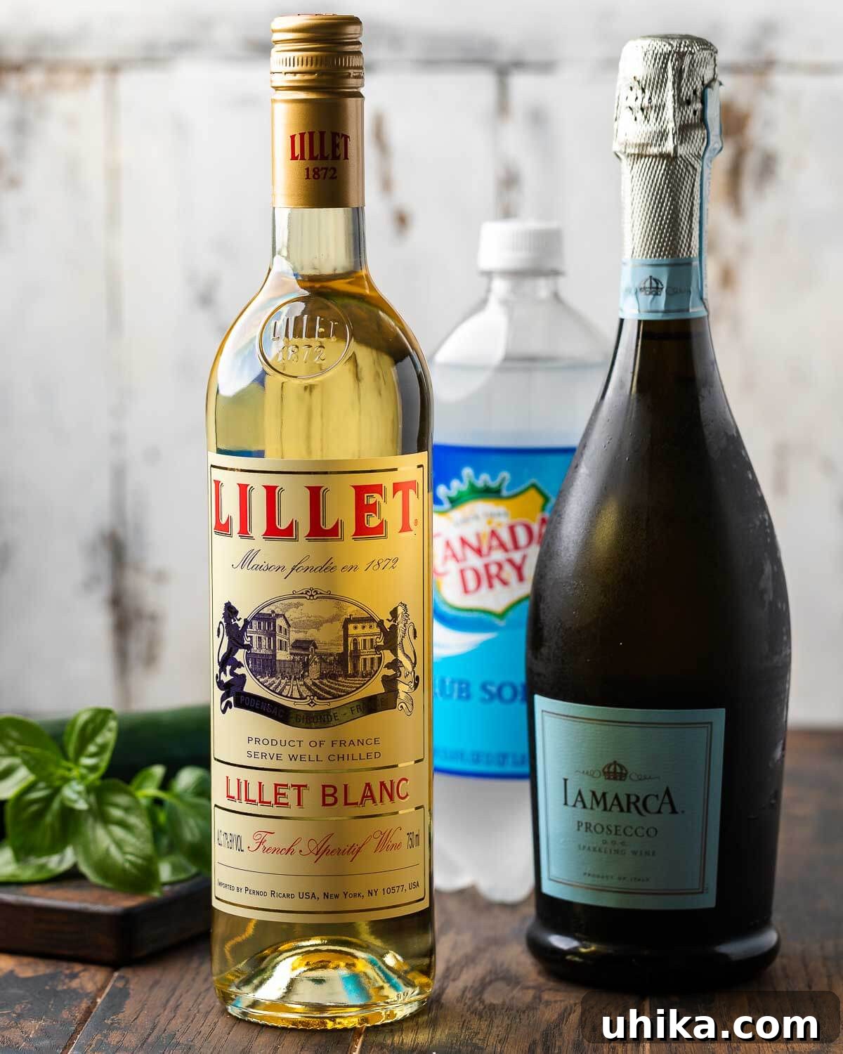 Effervescent Lillet Bliss 3 Essential Lillet Spritz ingredients laid out: Lillet Blanc bottle, Prosecco bottle, club soda can, fresh basil leaves, and cucumber slices.
