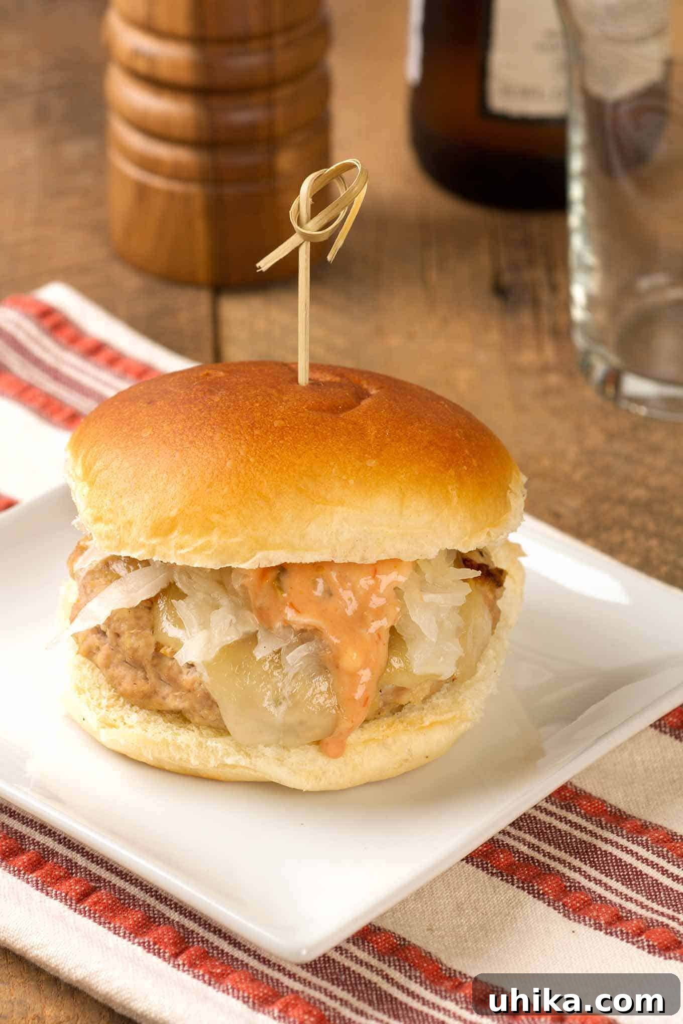 Reubenized Turkey Burger 2 A square white plate atop a striped tea towel with a Reuben-style turkey burger topped with melted Swiss cheese, sauerkraut, and thousand island dressing,
