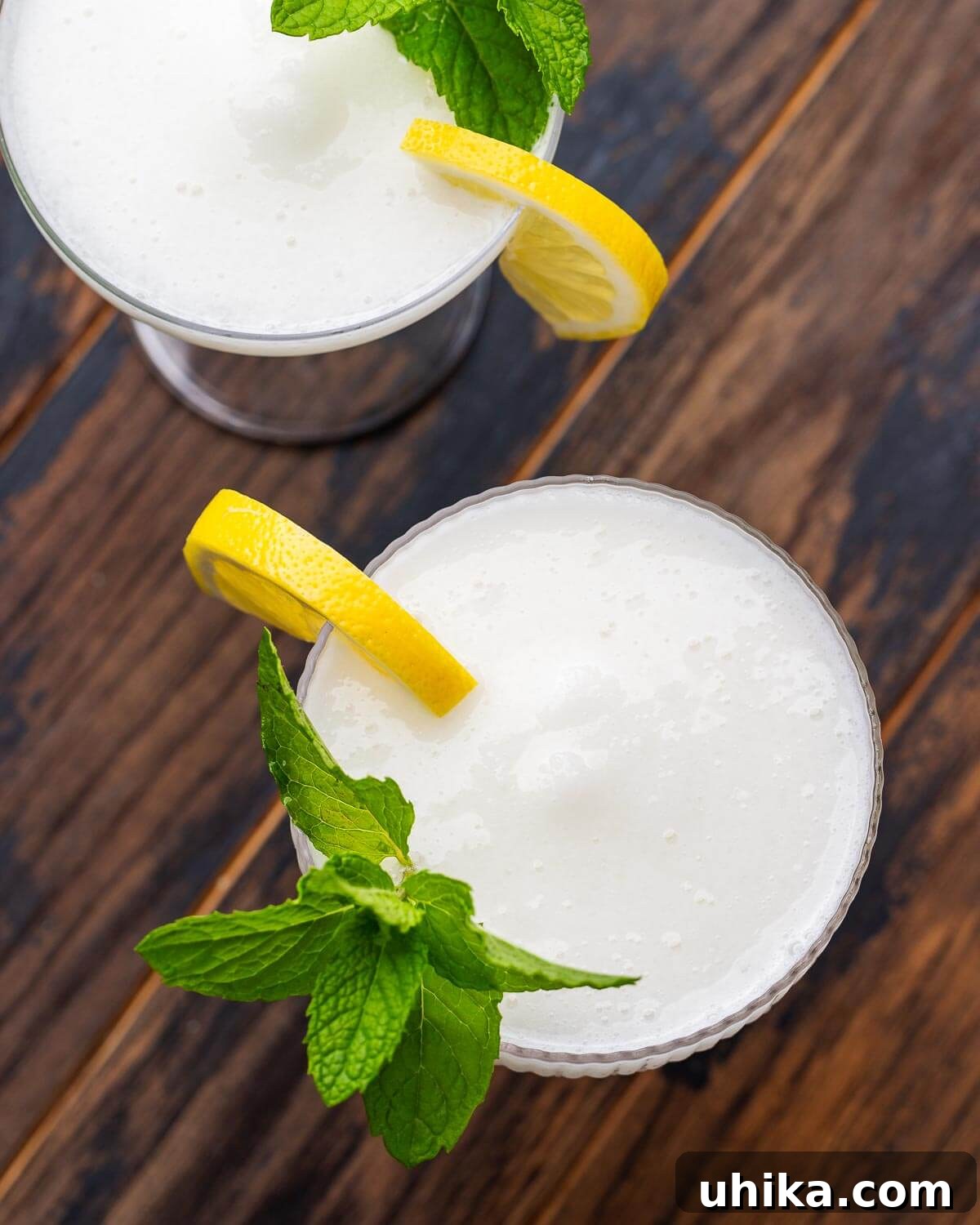 Sparkling Lemon Sorbetto 4 Overhead shot of two Sgroppino cocktails in coupe glasses, garnished with lemon wedges and mint leaves, on a wooden table.