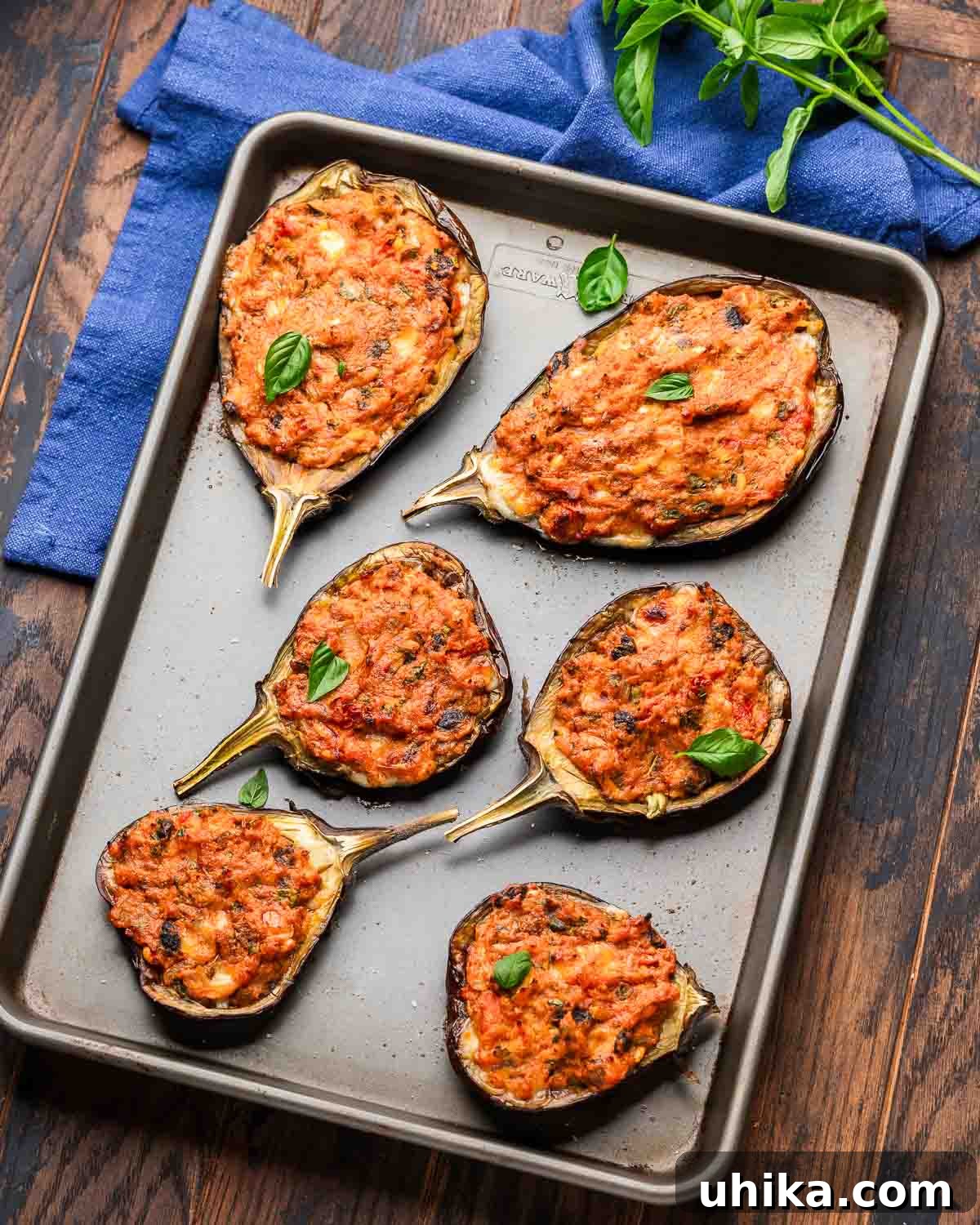 Hearty Stuffed Eggplant Boats 7 Overhead shot of Sicilian stuffed eggplant on baking sheet with blue napkin and basil, ready to serve.