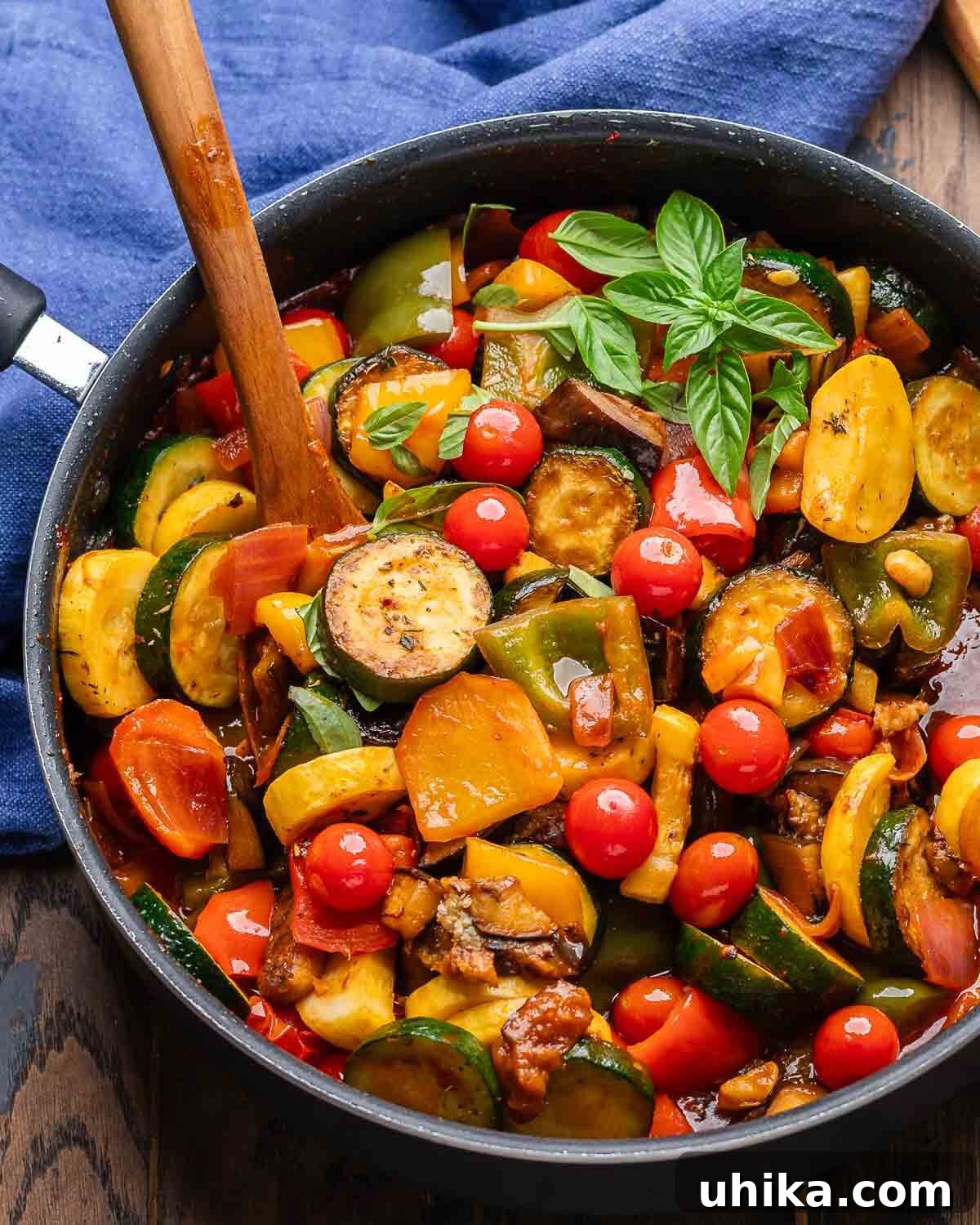 Vibrant Ratatouille stew in a black pan, served with a wooden spoon and a blue napkin.