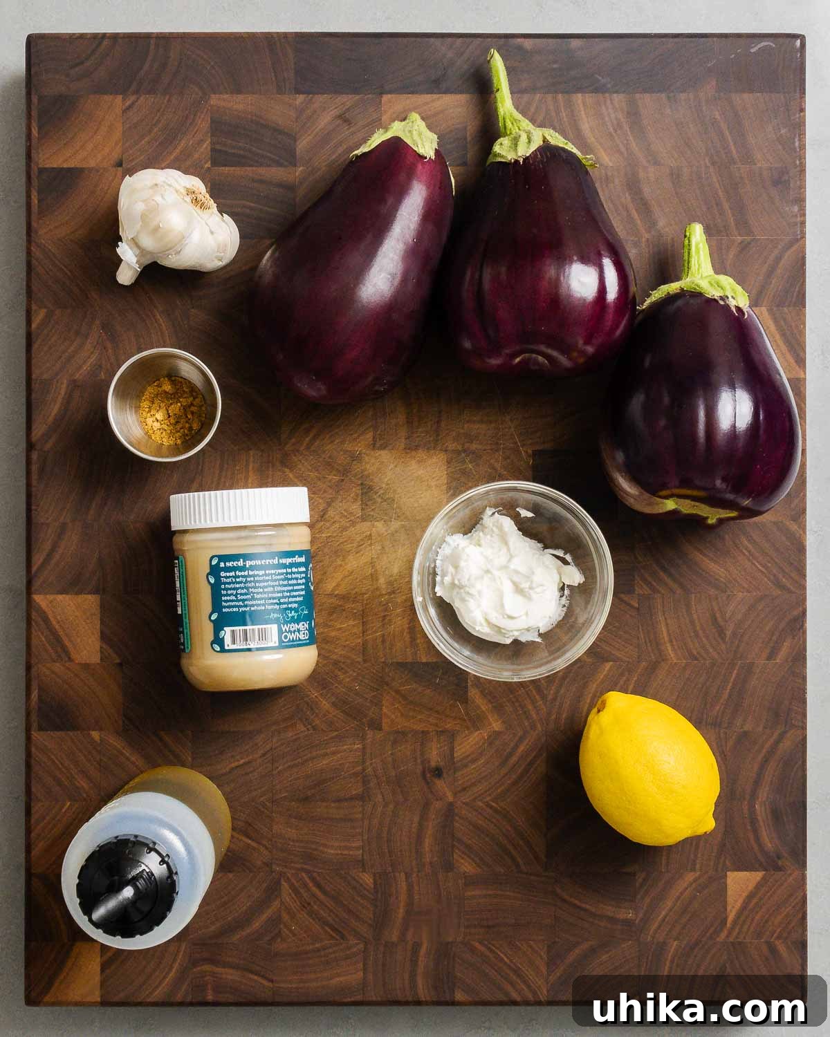 Ingredients shown: garlic, eggplants, cumin, tahini, Greek yogurt, extra virgin olive oil, and a lemon. Ready to be transformed into Baba Ganoush.