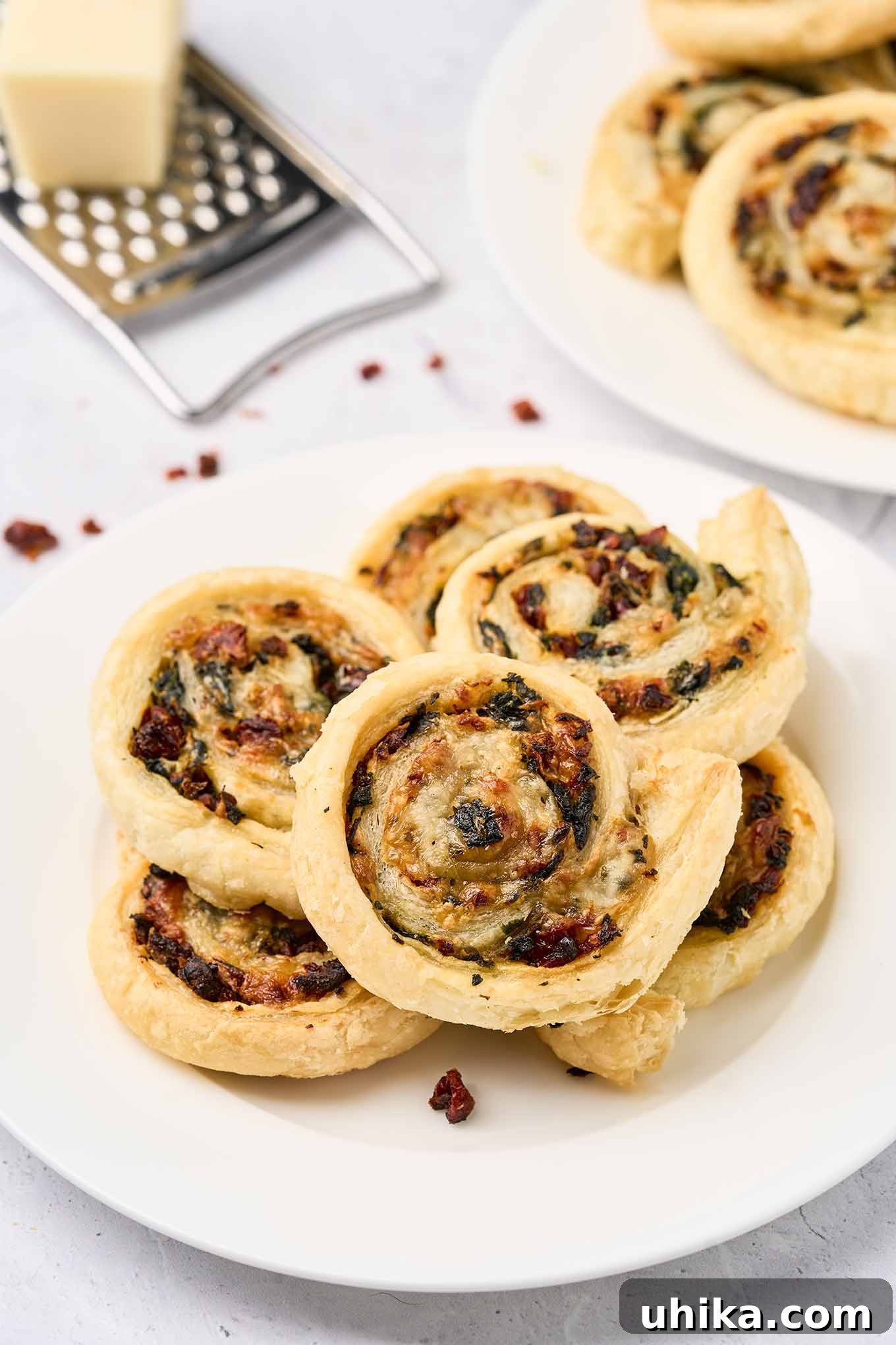 Savory Spinach Swirls 2 Golden spinach pinwheels made with puff pastry, spinach, sun-dried tomatoes, and cheese, stacked on a white plate, ready to be enjoyed.