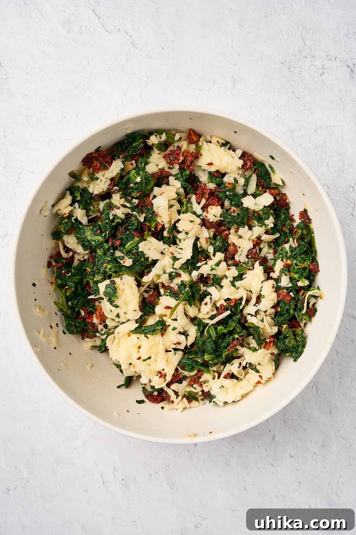 Savory Spinach Swirls 4 Spinach pinwheel filling mixture in a bowl ready for mixing; chopped spinach, sun-dried tomatoes, and grated fontina are visible, showcasing the key ingredients.