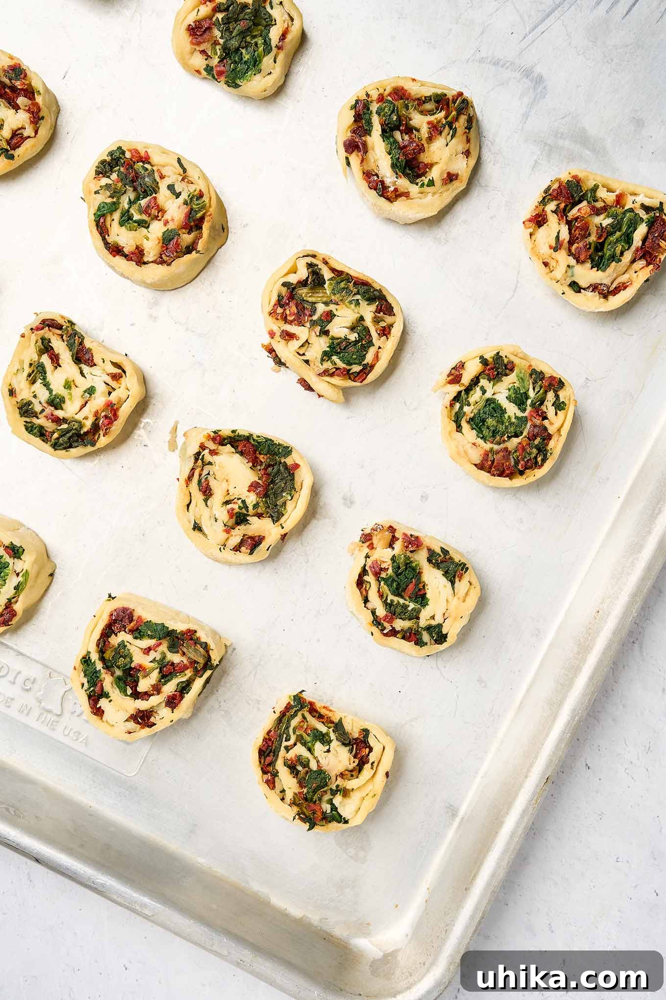 Savory Spinach Swirls 6 Sliced spinach pinwheel rounds arranged neatly on a parchment-lined baking sheet, spaced apart and ready to bake to golden perfection.